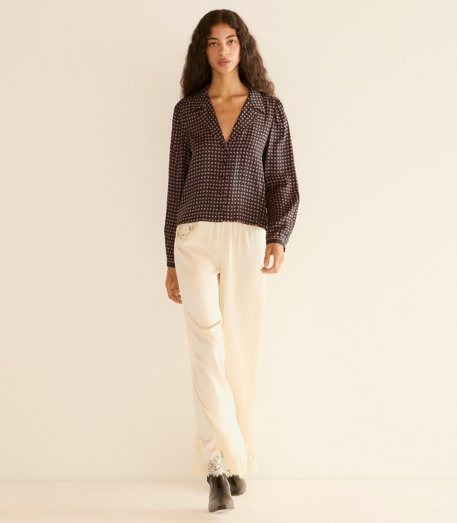 Woman wearing a black patterned blouse and beige pants on a beige background 2