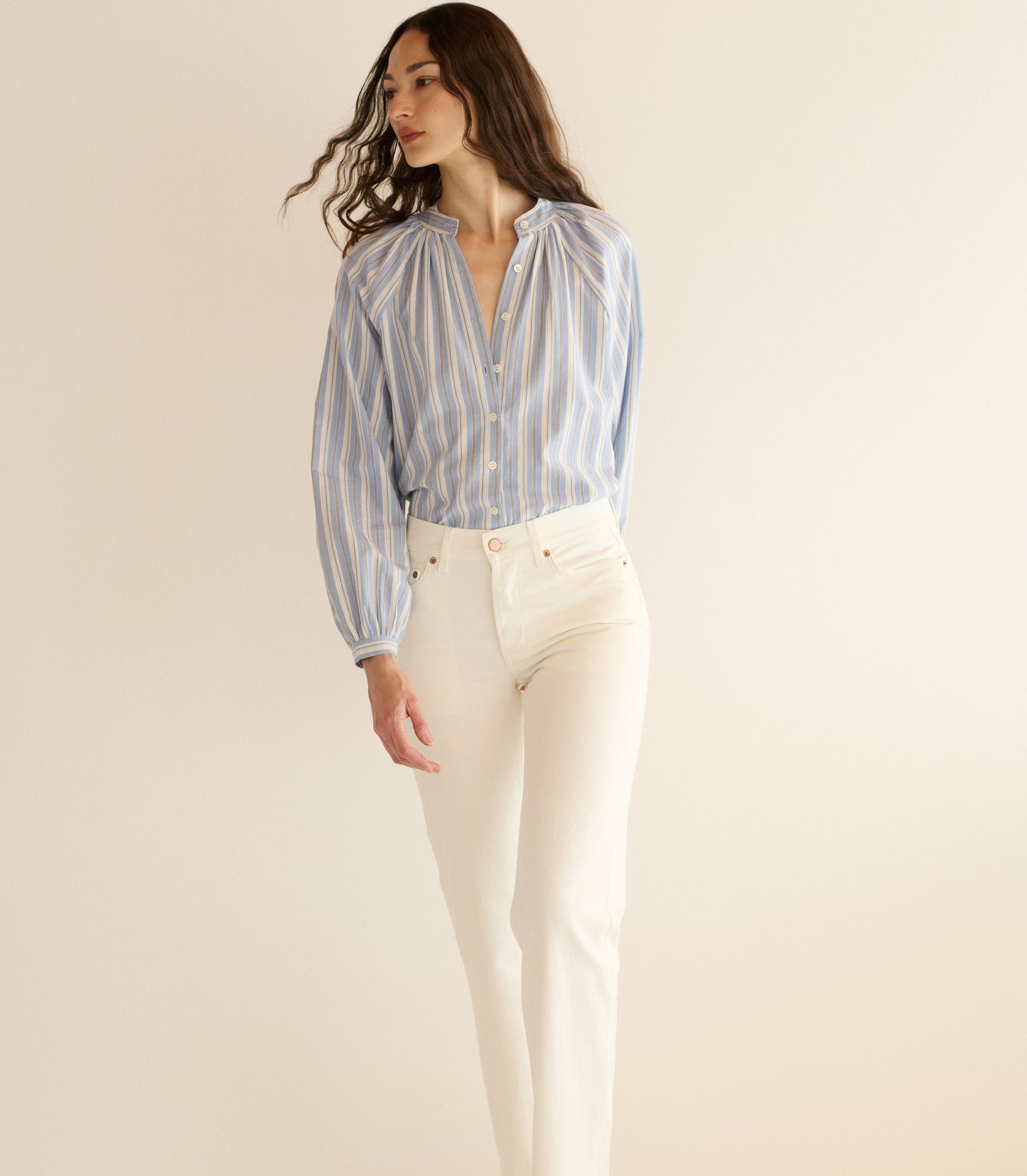 Woman wearing a striped shirt and white pants on a beige background