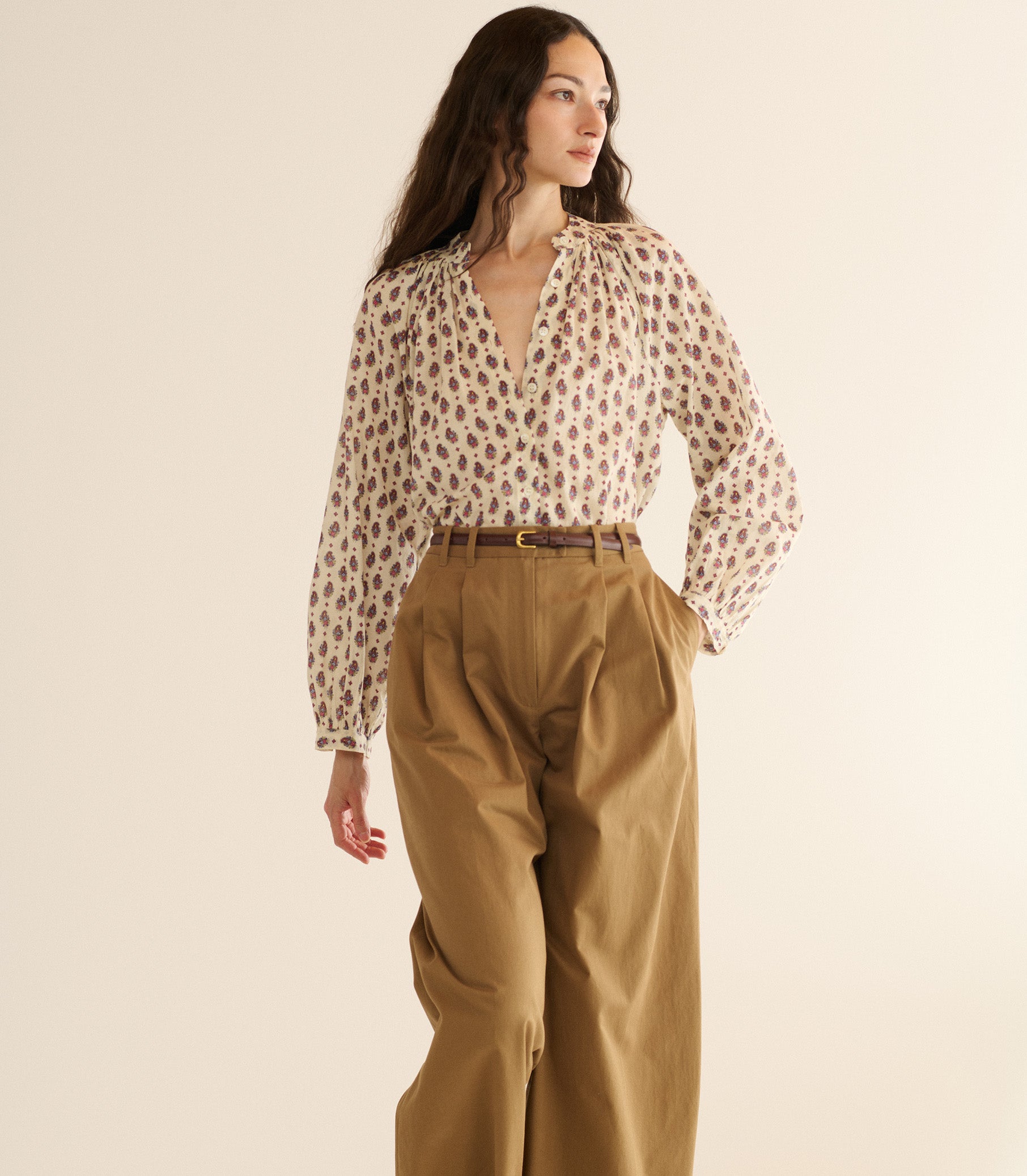 Woman wearing a patterned blouse and beige pants against a plain background 2