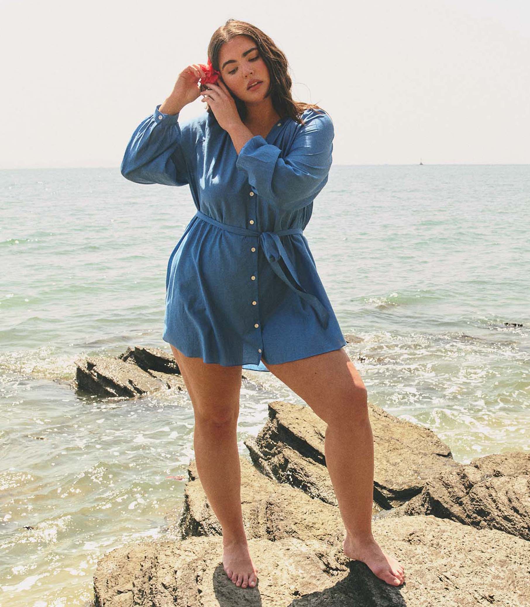 Woman in a blue dress standing on a rock by the ocean 1
