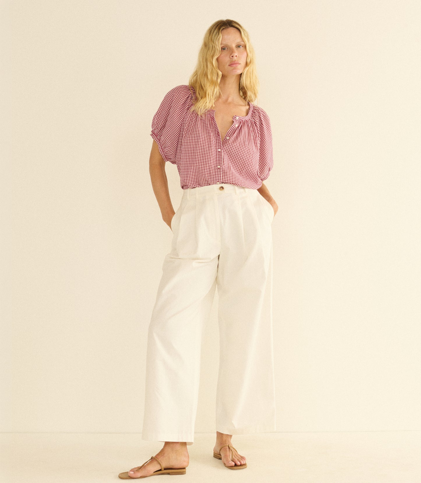 Woman wearing a red checkered blouse and white pants on a beige background