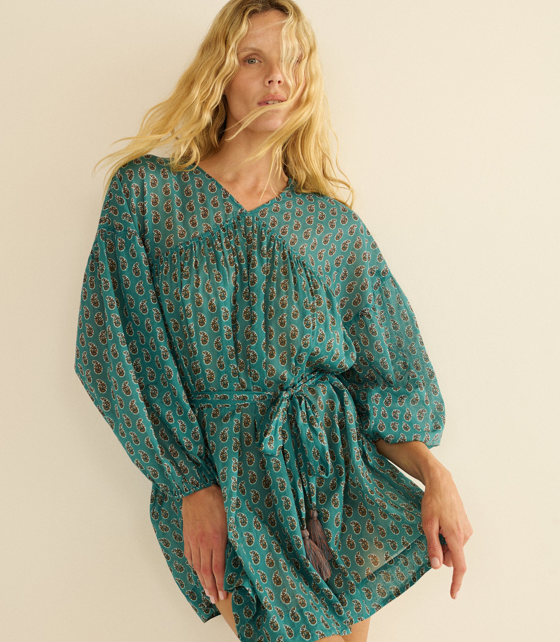 Woman wearing a teal patterned dress against a beige background 1
