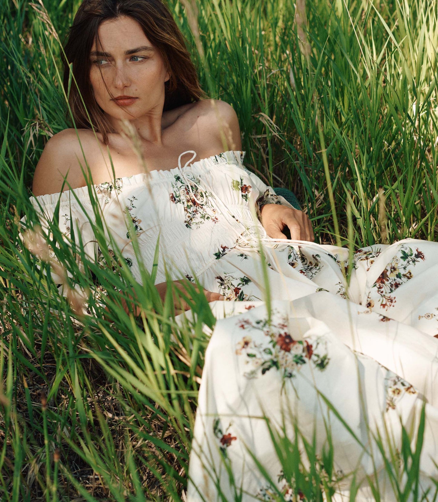 Woman in a white floral dress sitting in tall grass