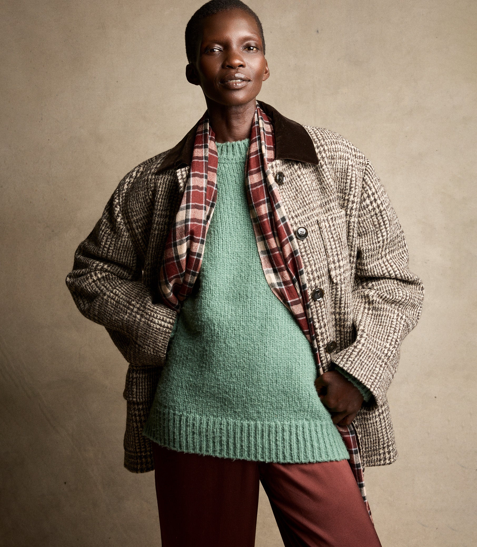 Person wearing a plaid coat over a green sweater and red pants on a beige background 5