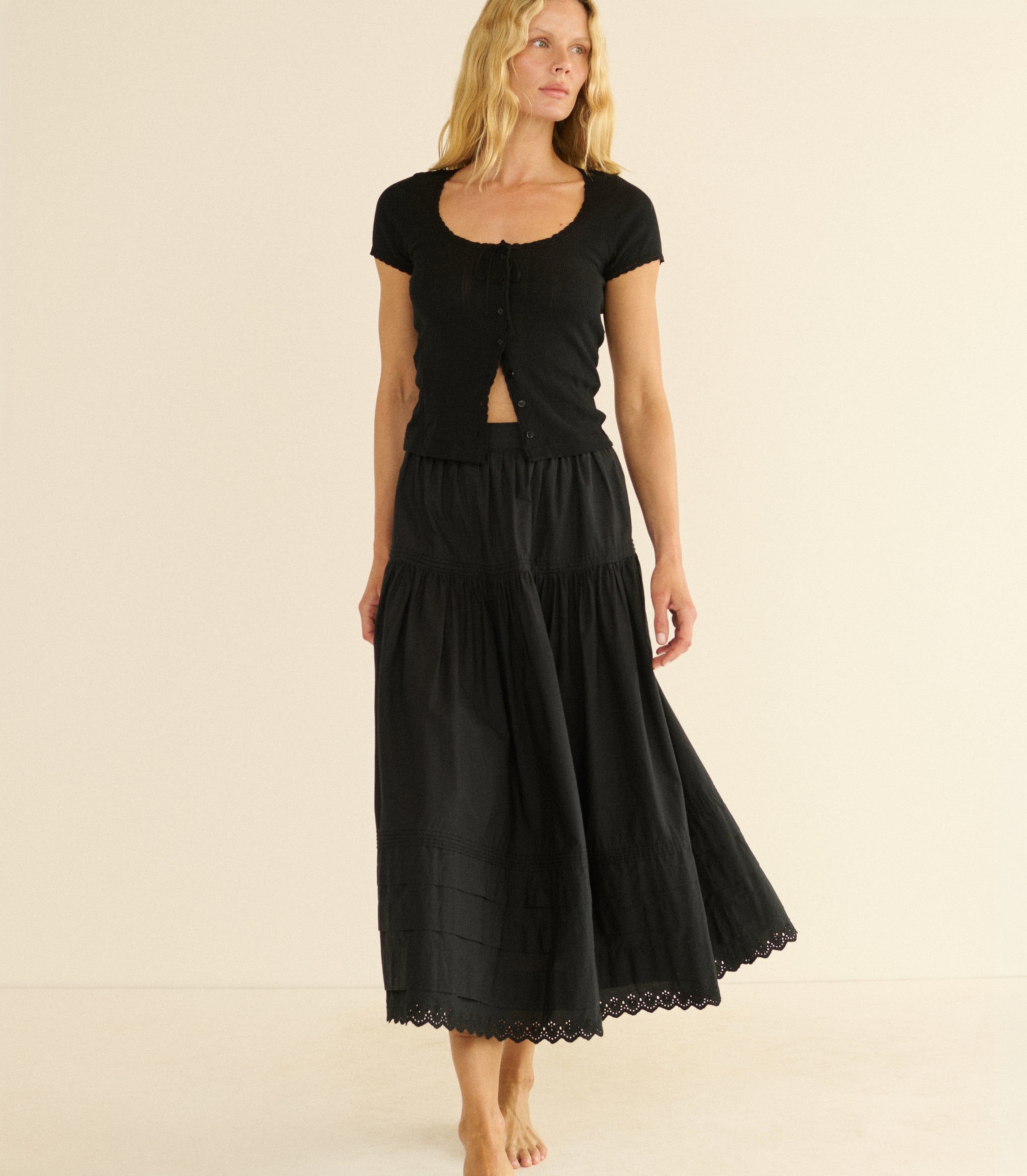 Woman wearing a black top and black maxi skirt on a beige background