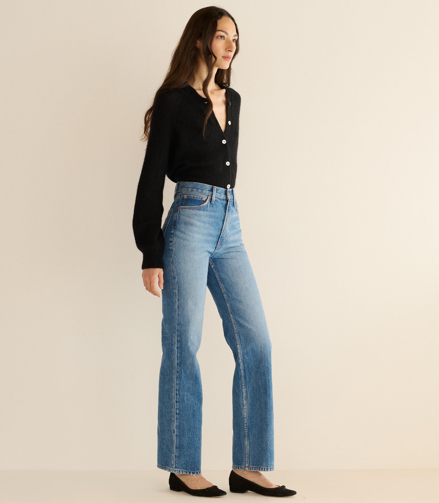 Woman wearing a black top and blue jeans on a beige background
