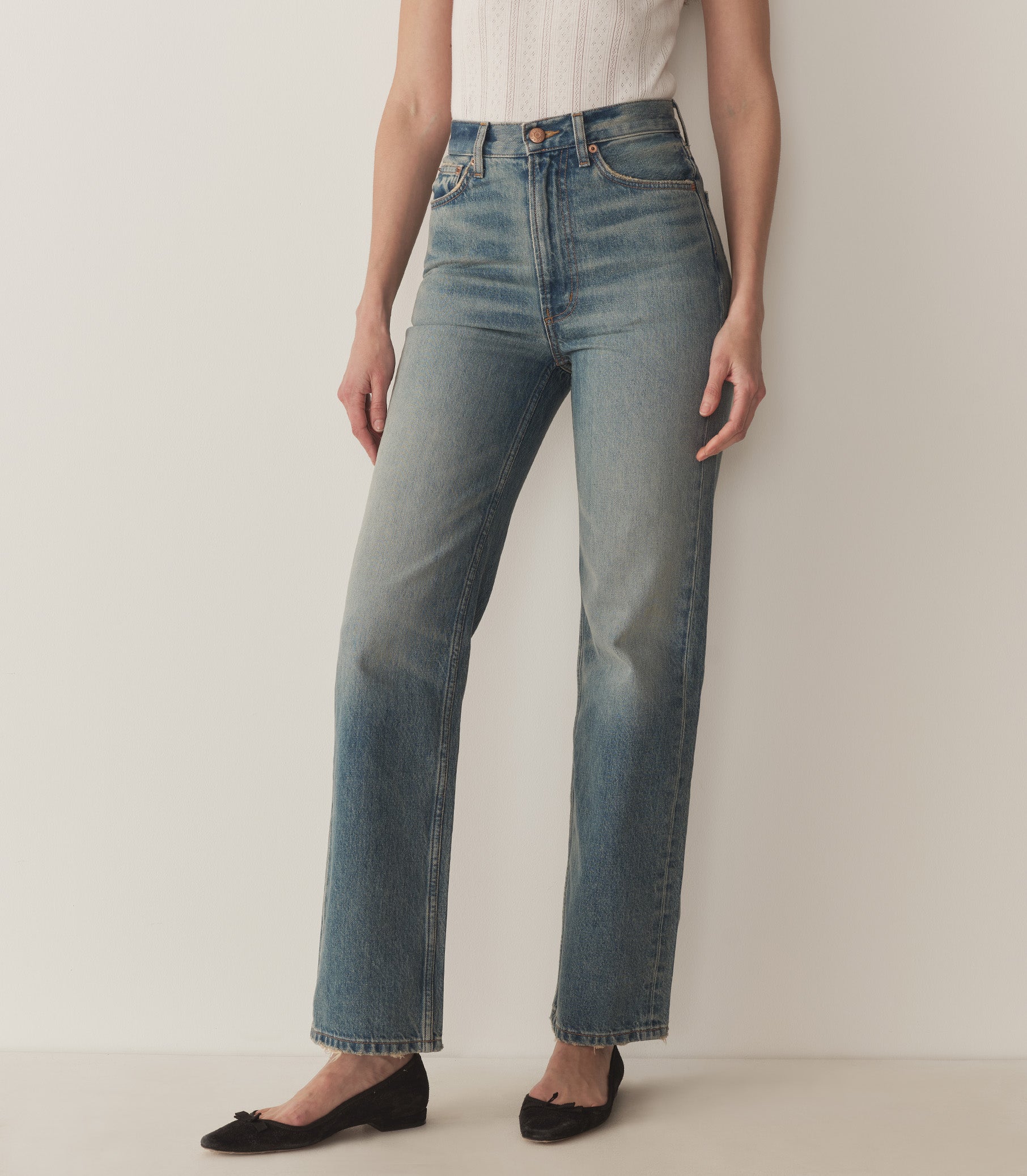 Bruna wears a white pointelle t-shirt, straight-fit jeans, and black ballet slippers. 1