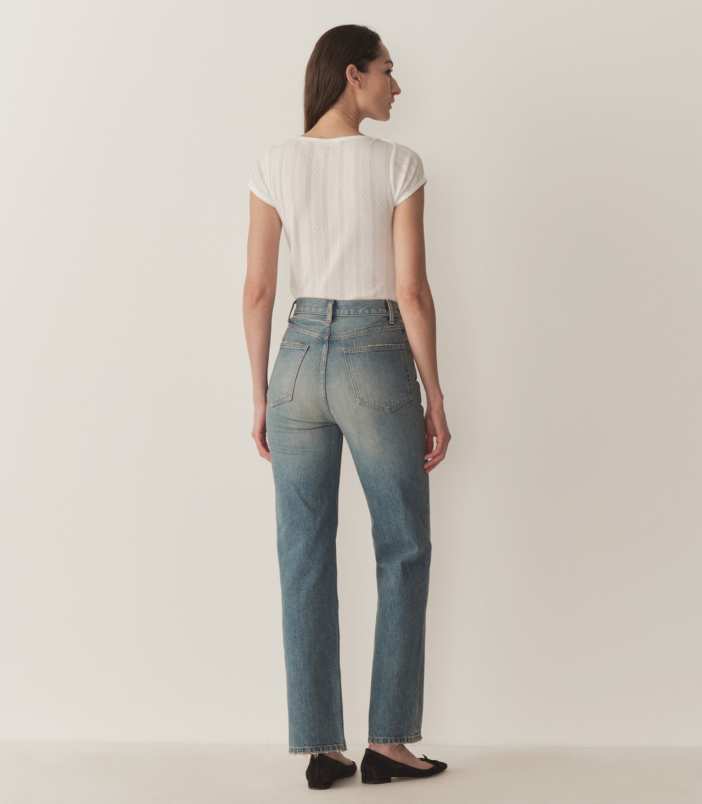 Bruna wears a white pointelle t-shirt, straight-fit jeans, and black ballet slippers.