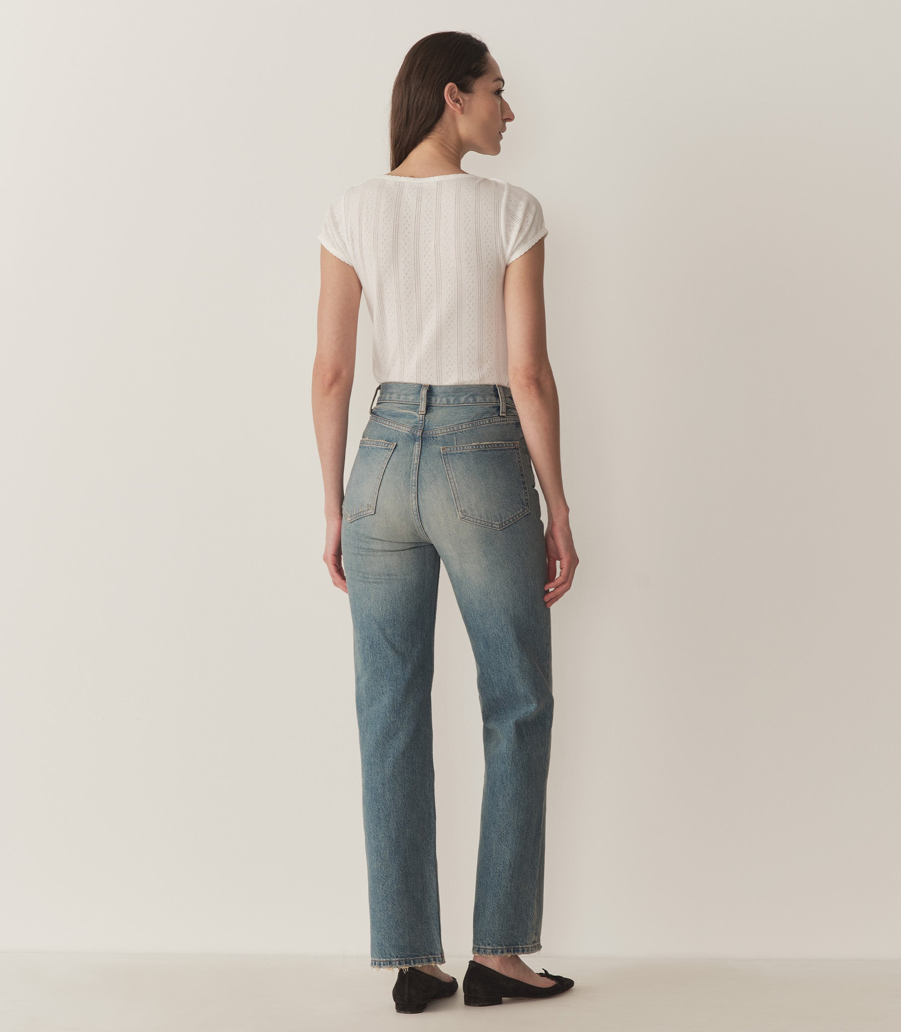 Bruna wears a white pointelle t-shirt, straight-fit jeans, and black ballet slippers. 3