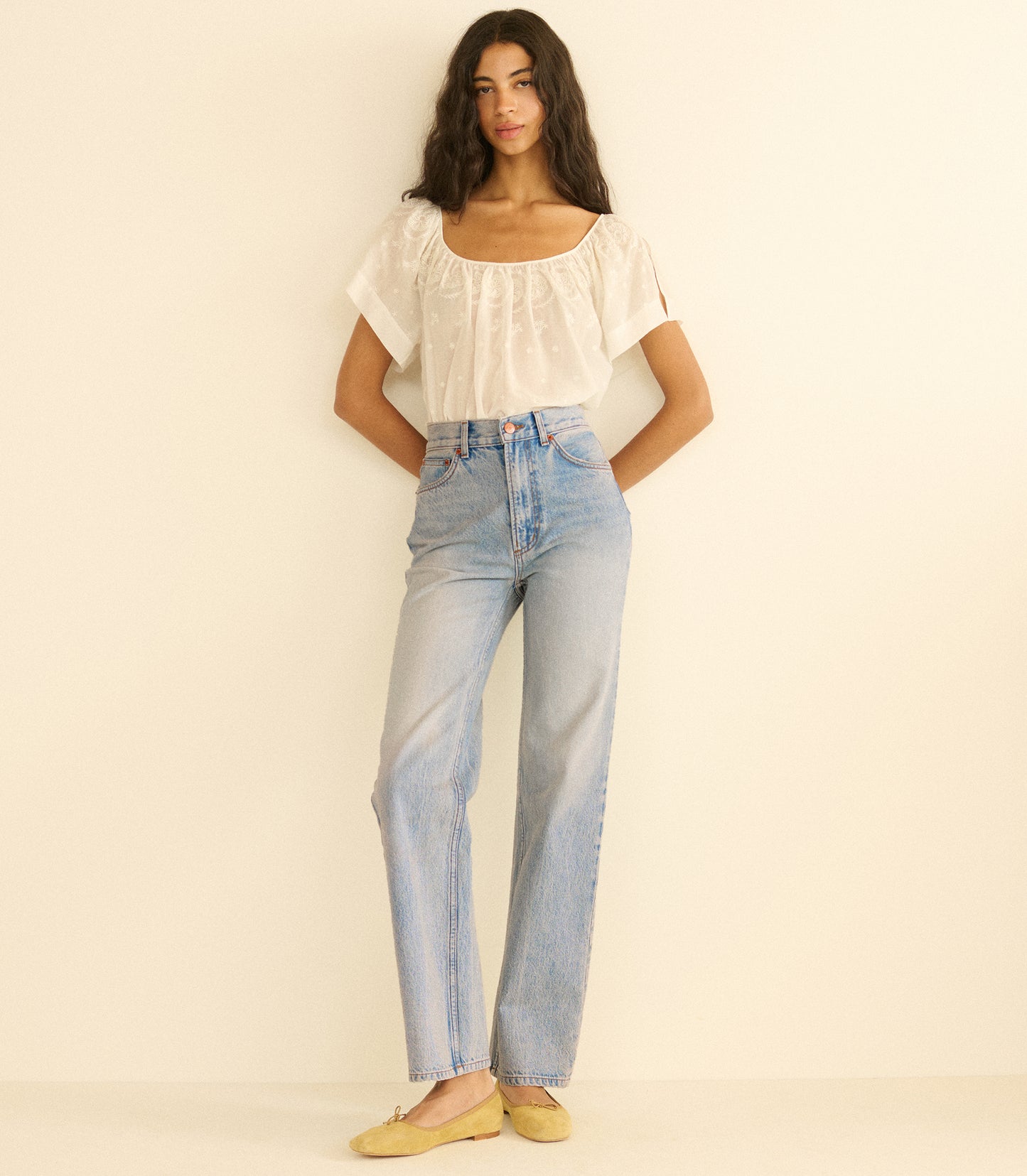 Woman wearing a white blouse and light blue jeans against a plain background