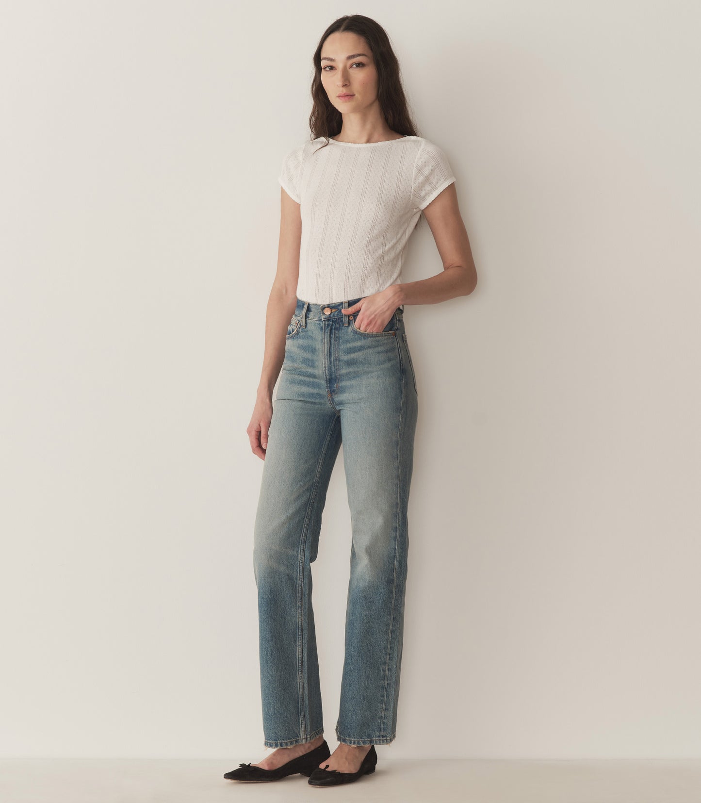 Bruna wears a white pointelle t-shirt, straight-fit jeans, and black ballet slippers.