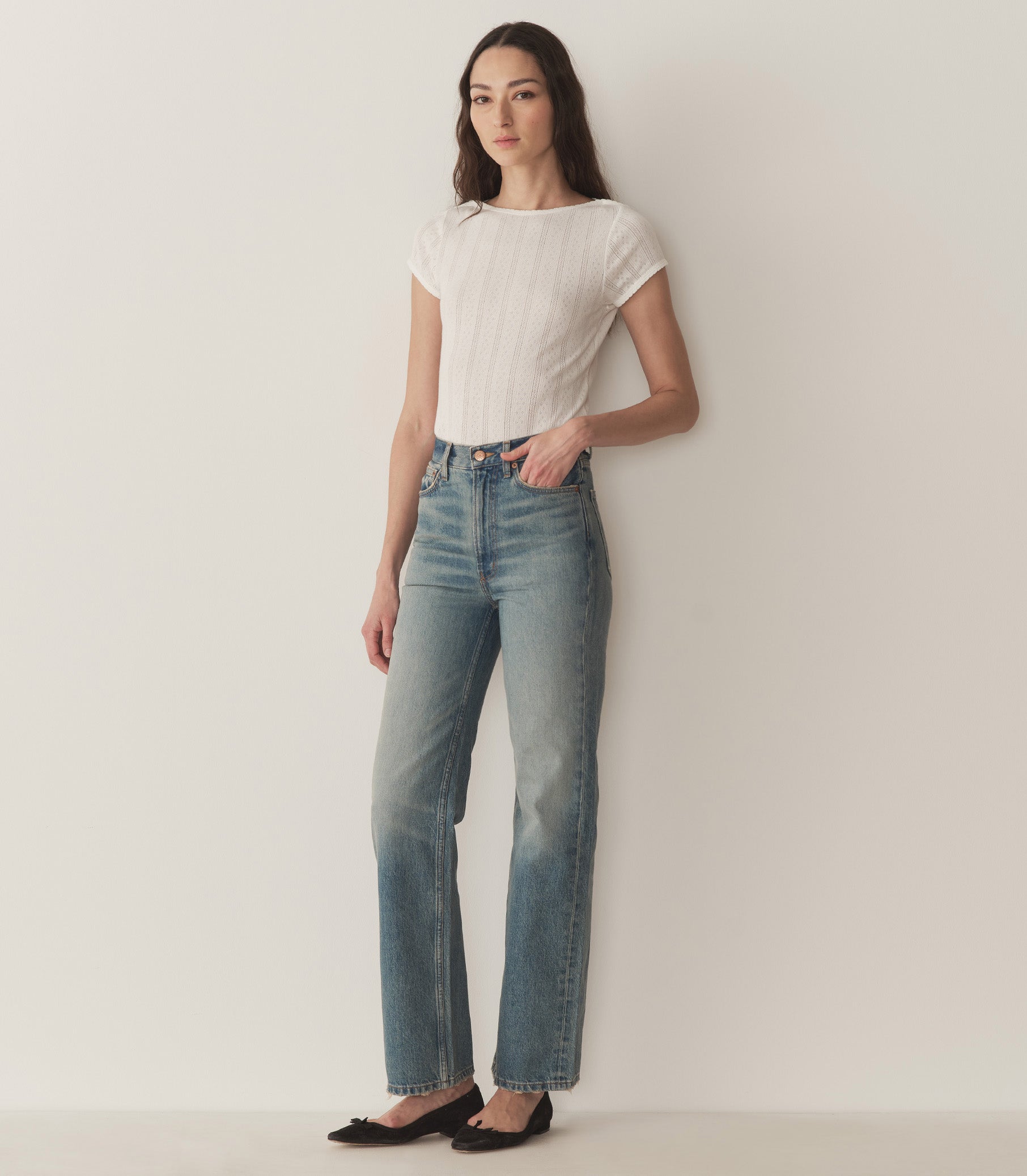 Bruna wears a white pointelle t-shirt, straight-fit jeans, and black ballet slippers. 2