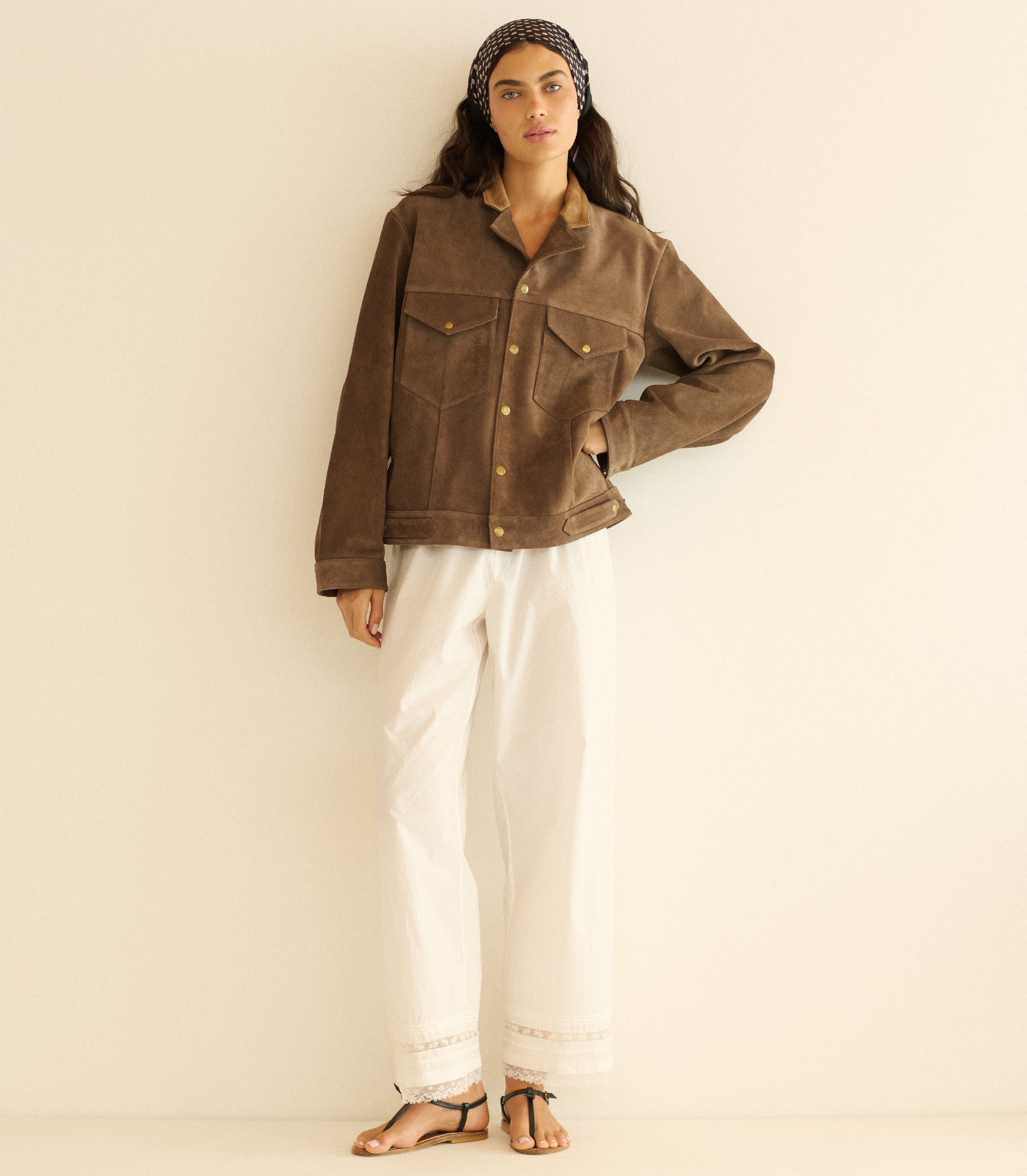 Woman wearing a brown jacket and white pants against a plain background 1
