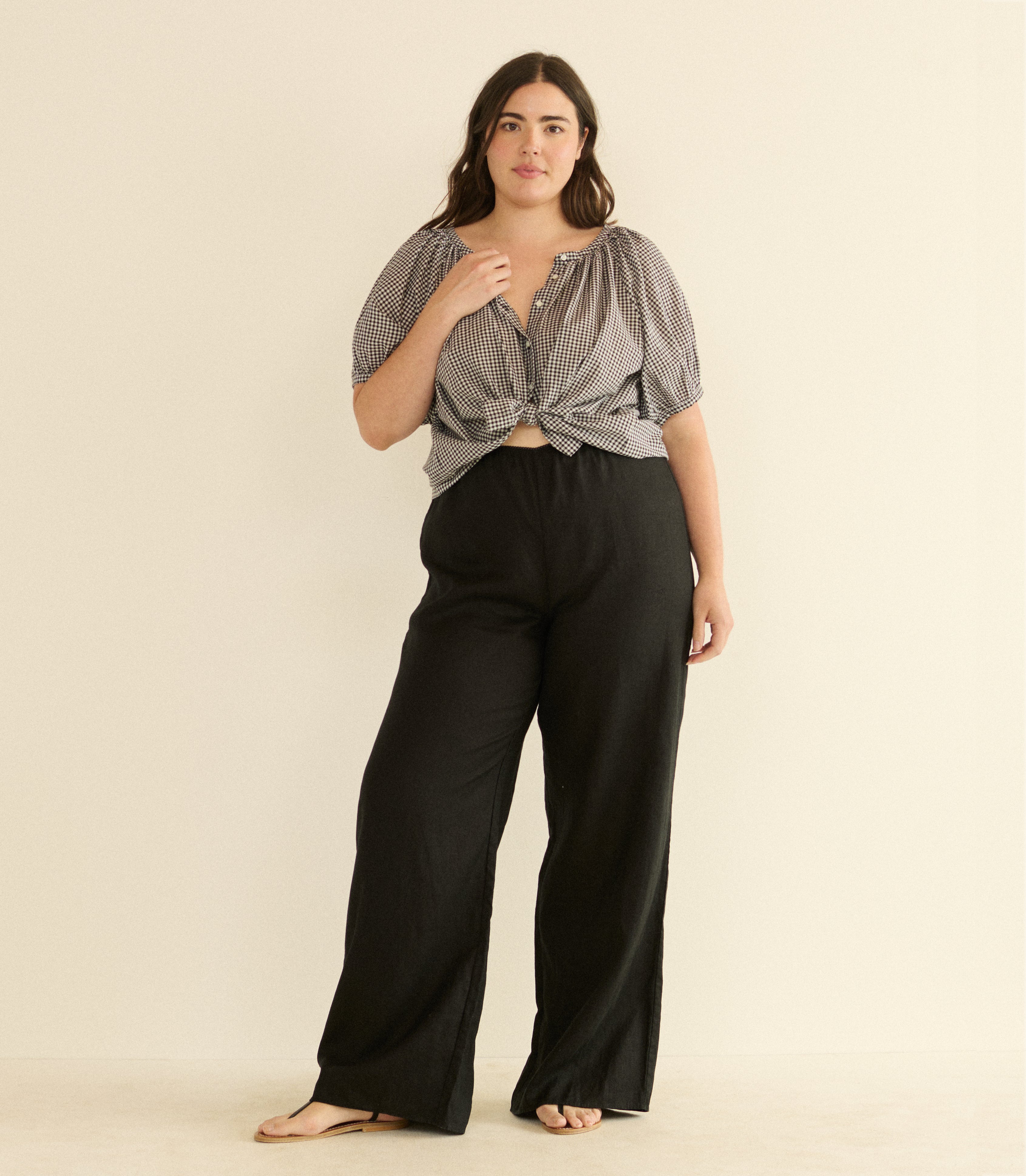 Woman wearing a black and white checkered top and black pants on a beige background