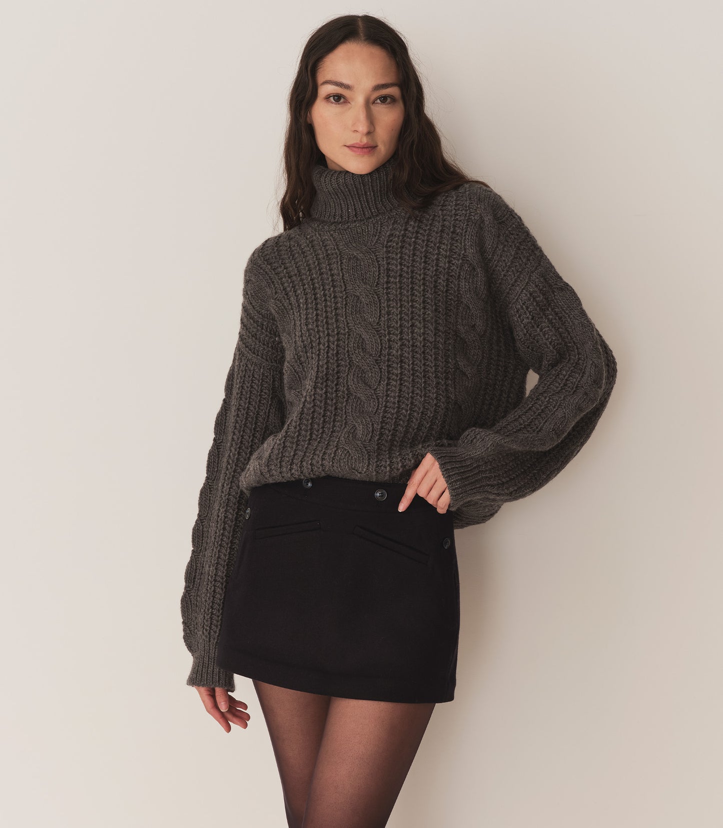 Person wearing a dark grey turtleneck sweater and a navy blue skirt with tights.