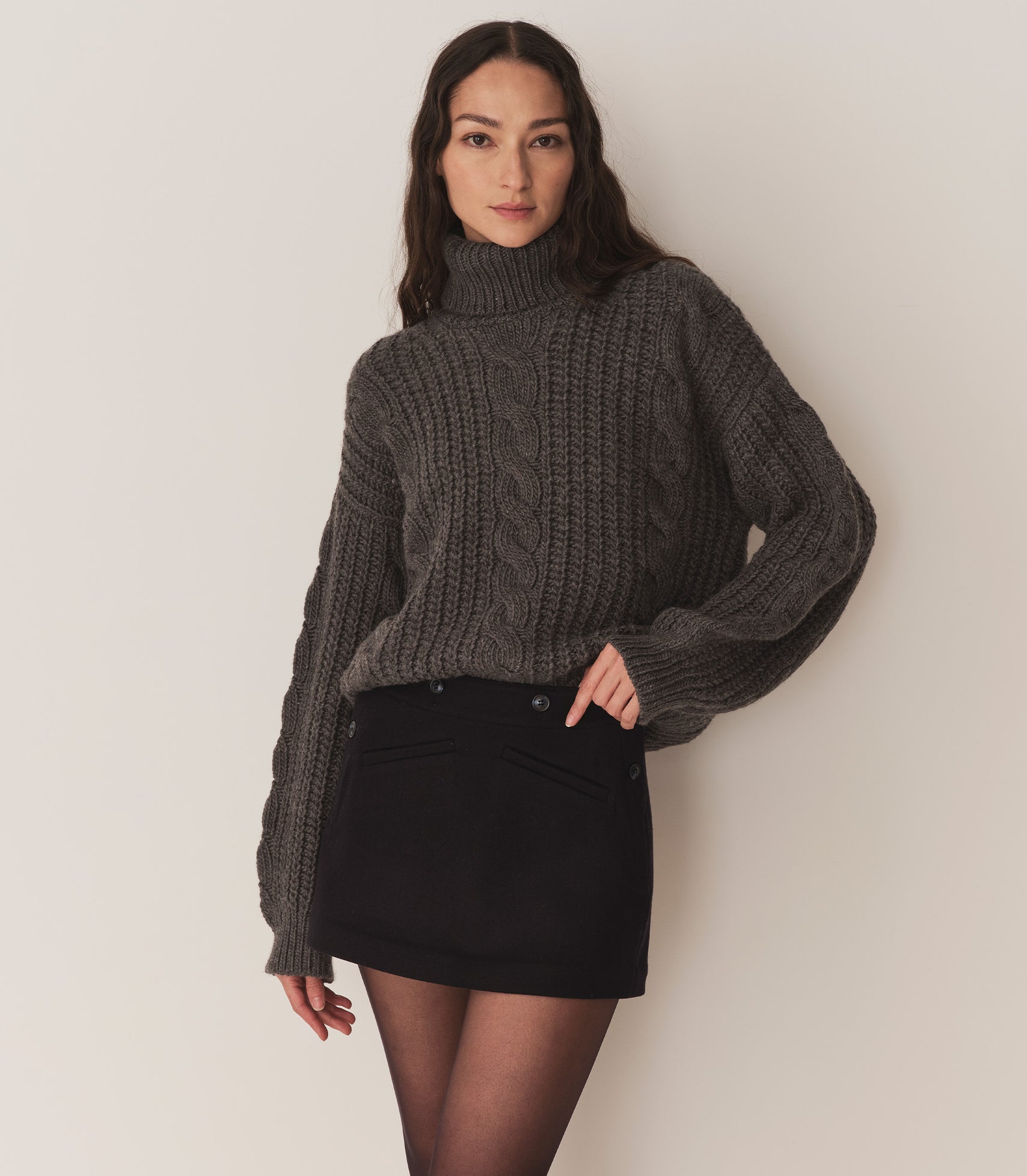 Person wearing a dark grey turtleneck sweater and a navy blue skirt with tights.