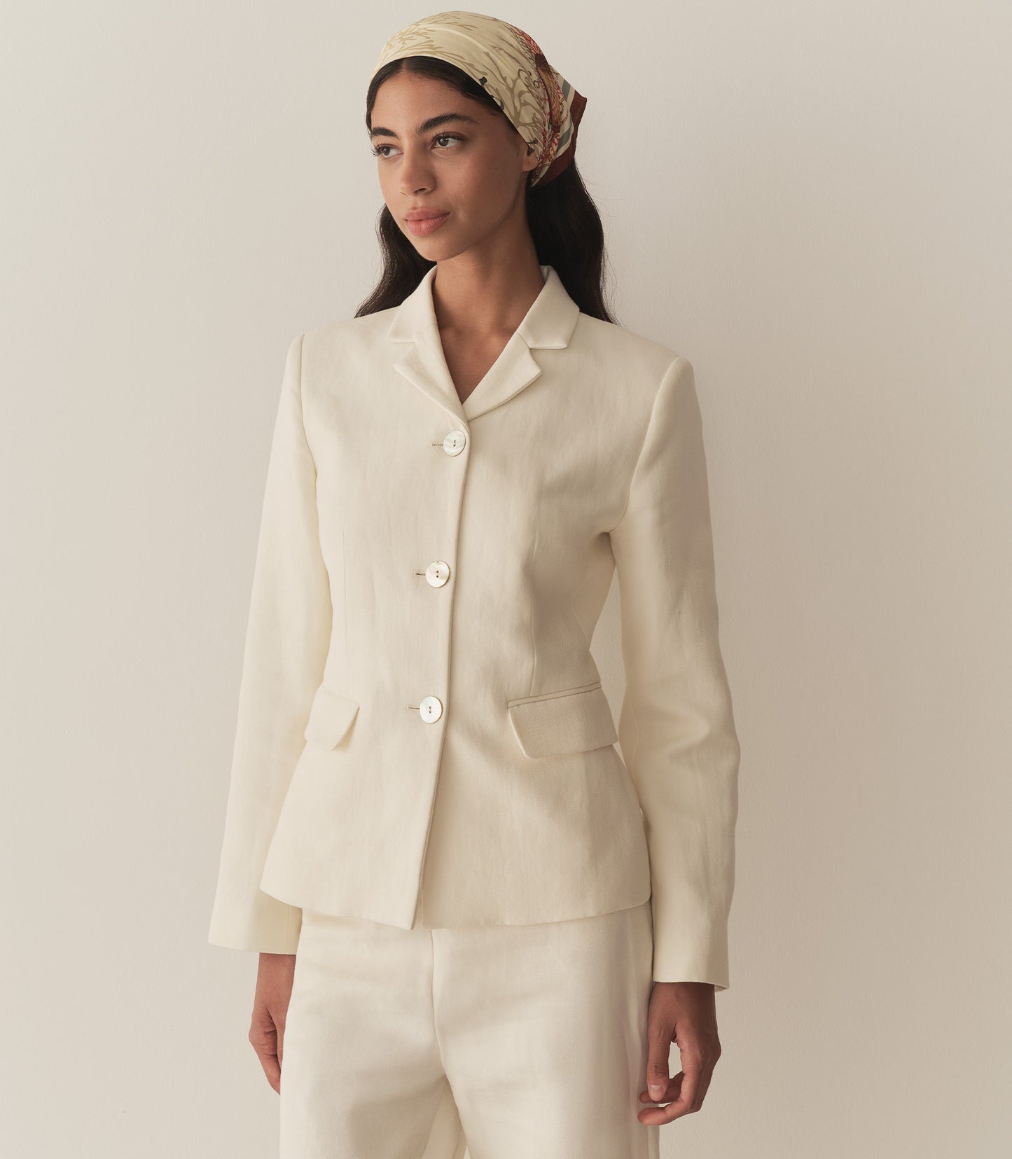 Rocio is wearing an off white blazer paired with its matching pants, a bandana, and brown kitten mules.