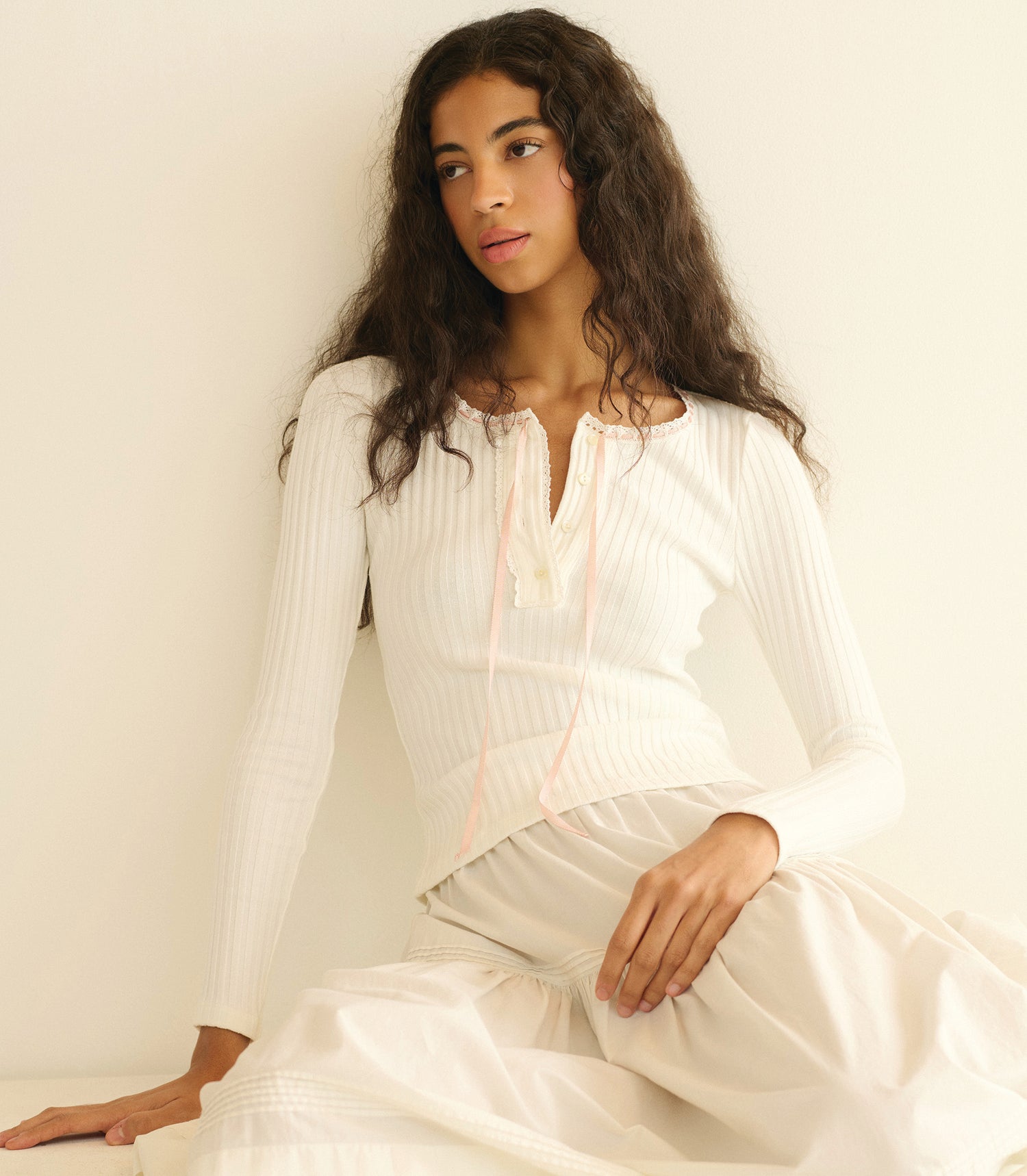 Woman wearing a white knit tee sitting against a plain background