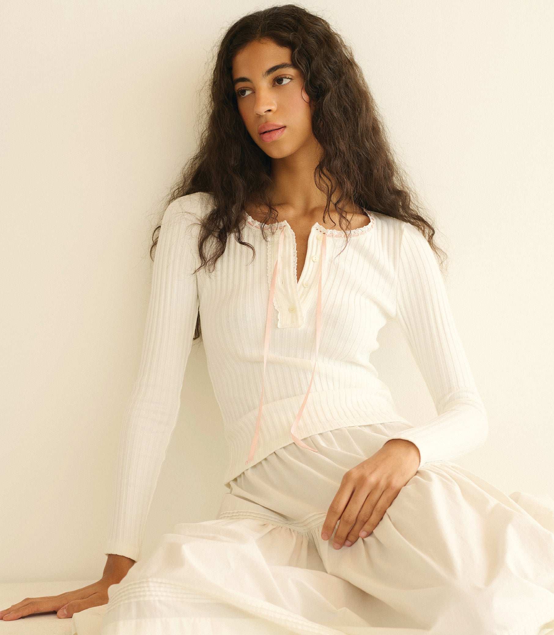 Woman wearing a white knit tee sitting against a plain background