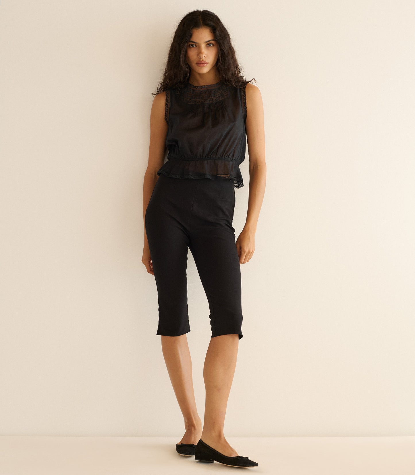 Woman wearing a black sleeveless top with lace details against a beige background