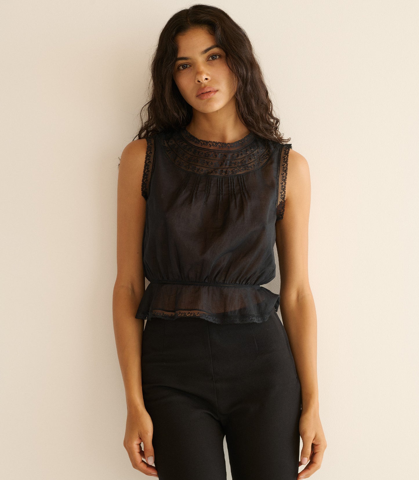 Woman wearing a black sleeveless top with lace details against a beige background