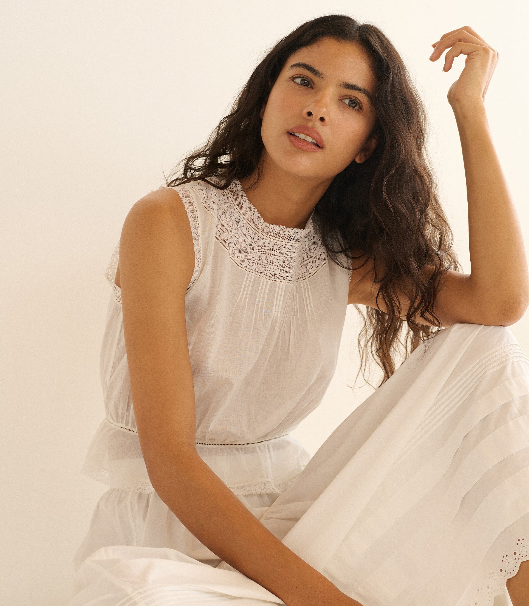 Woman wearing a white dress with intricate detailing against a plain background 1