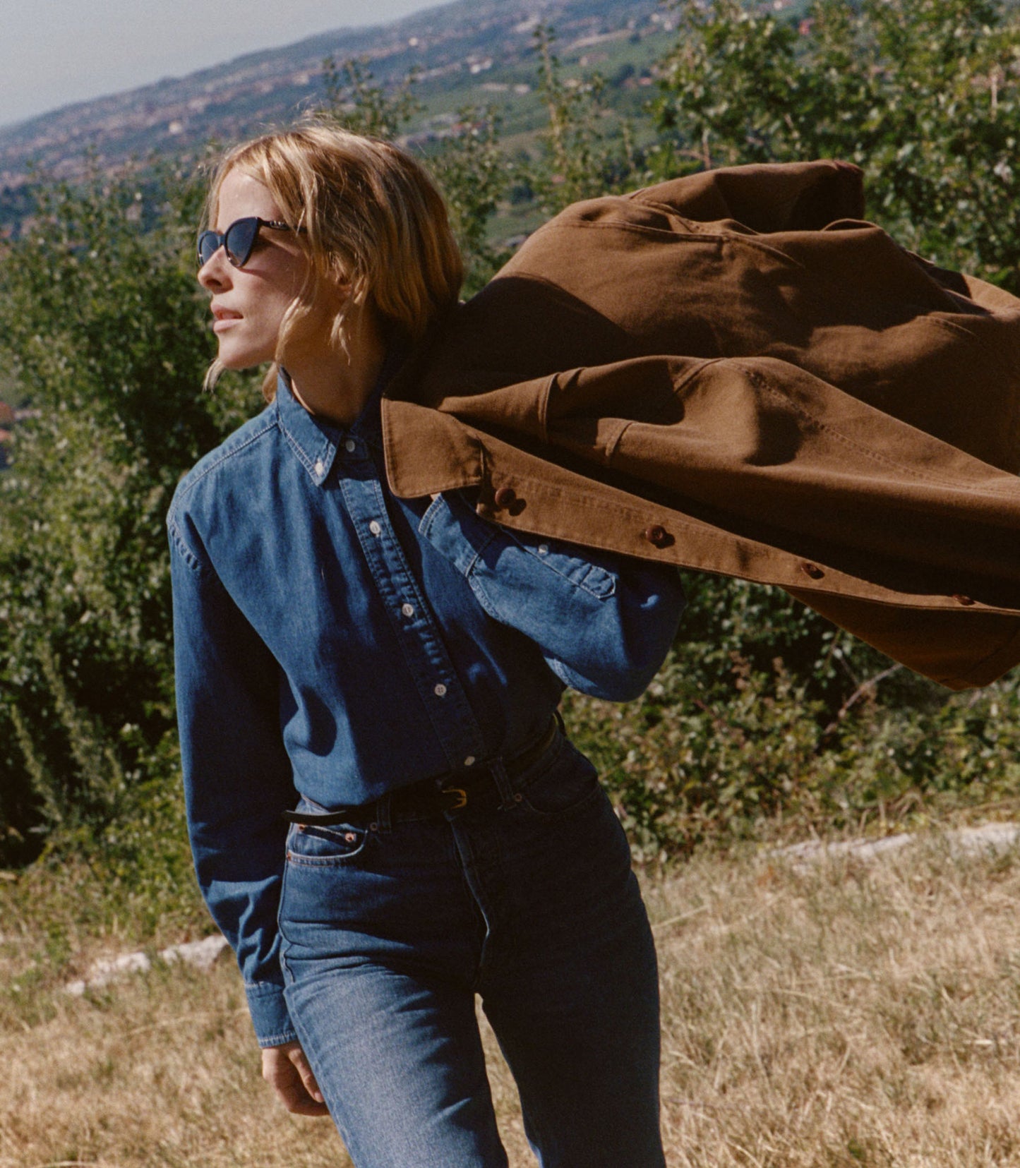 Person carrying a brown jacket over their shoulder in an outdoor setting