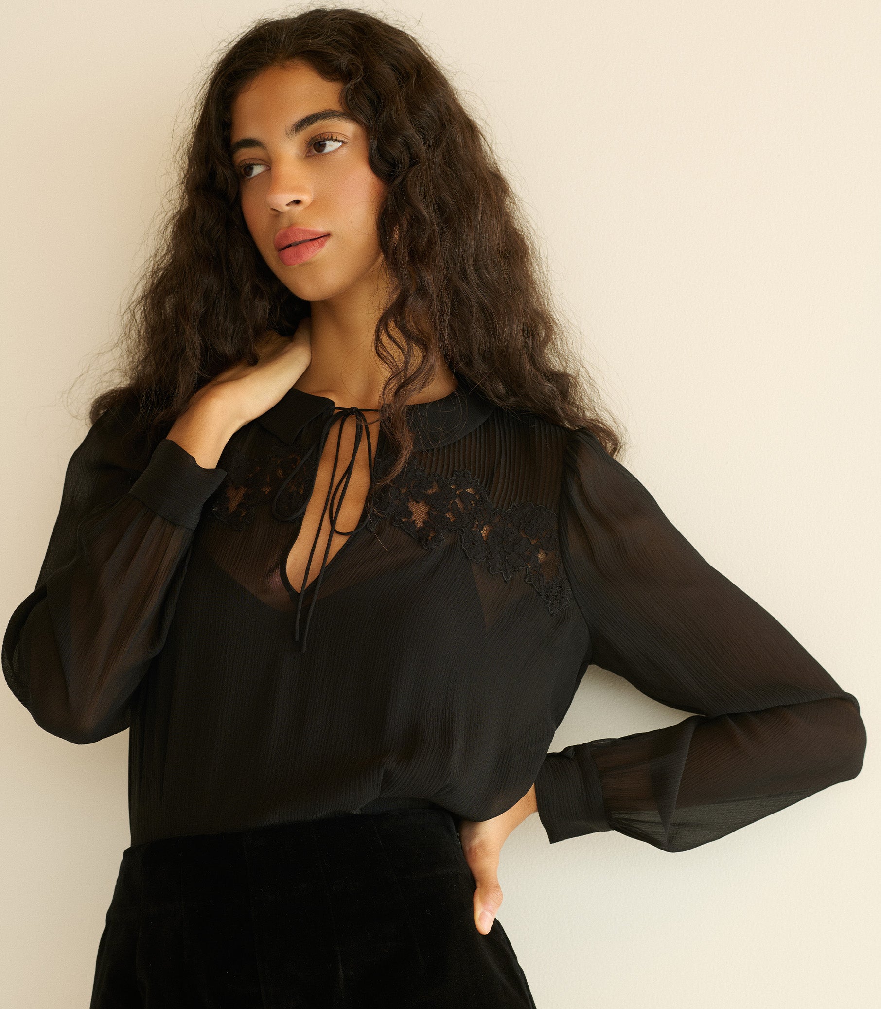 Woman wearing a black blouse with sheer sleeves against a plain background 1