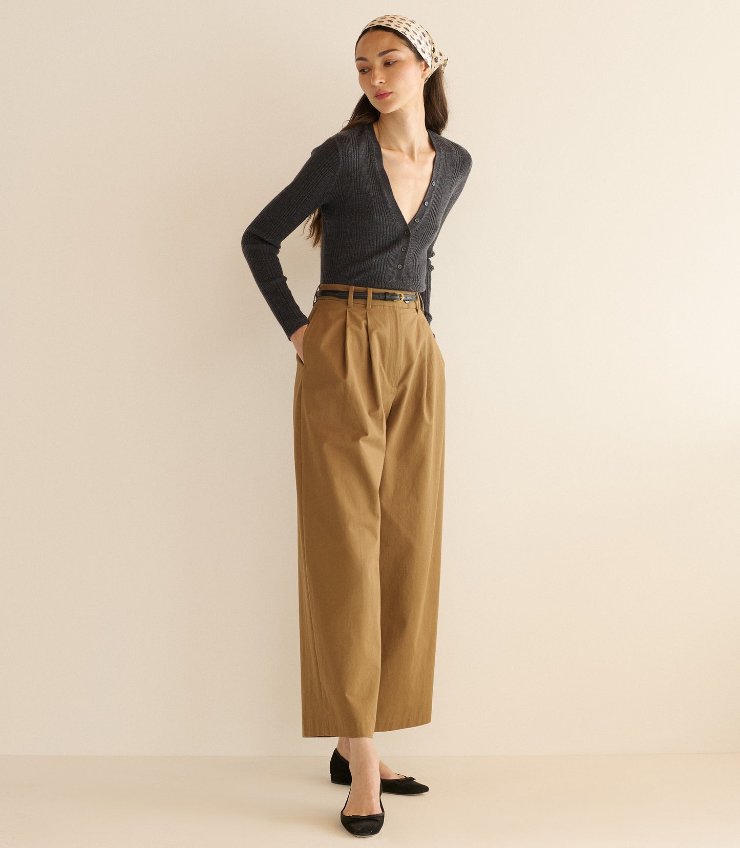 Woman wearing a dark blue cardigan and tan pants against a beige background