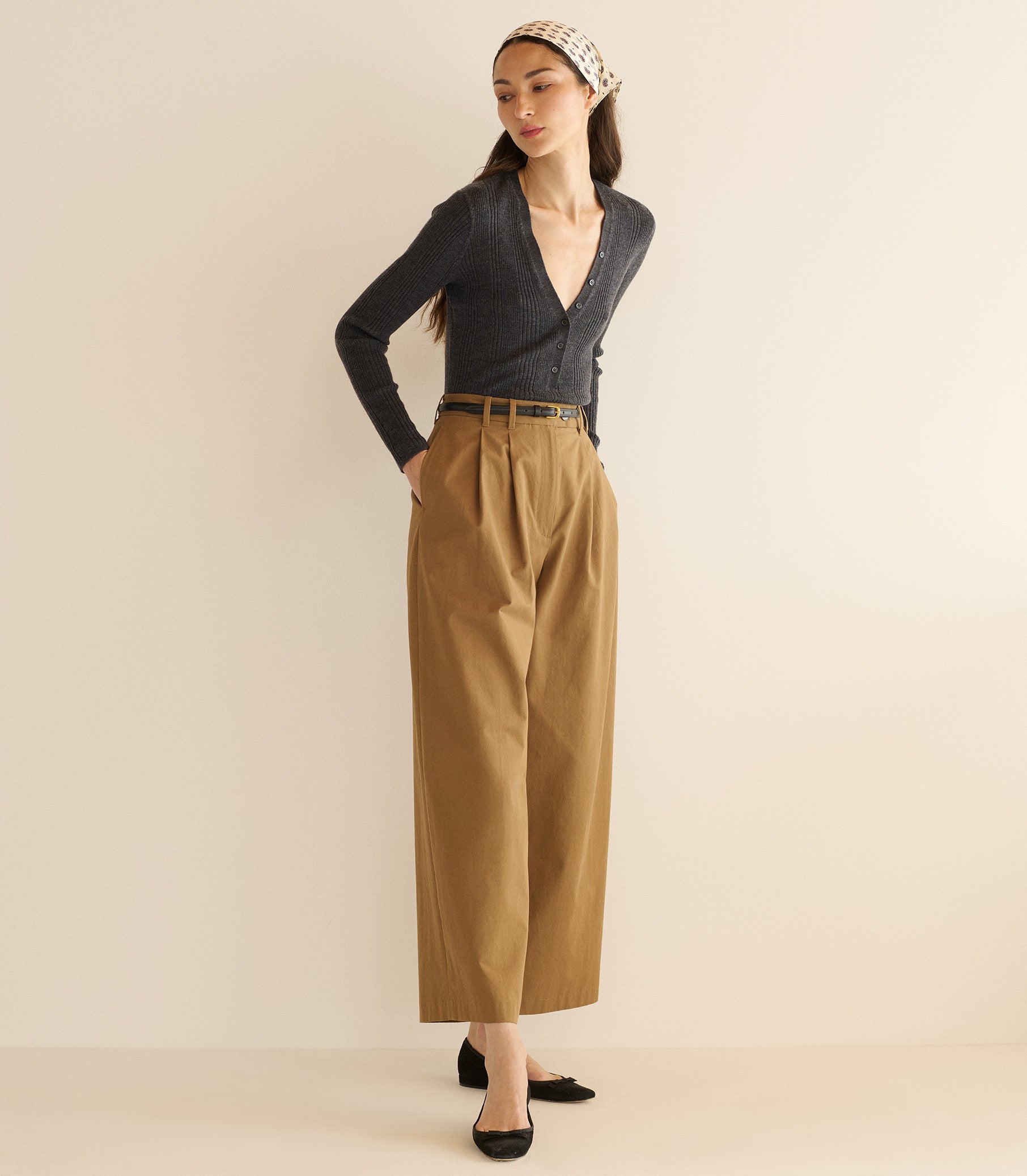 Woman wearing a dark blue cardigan and tan pants against a beige background