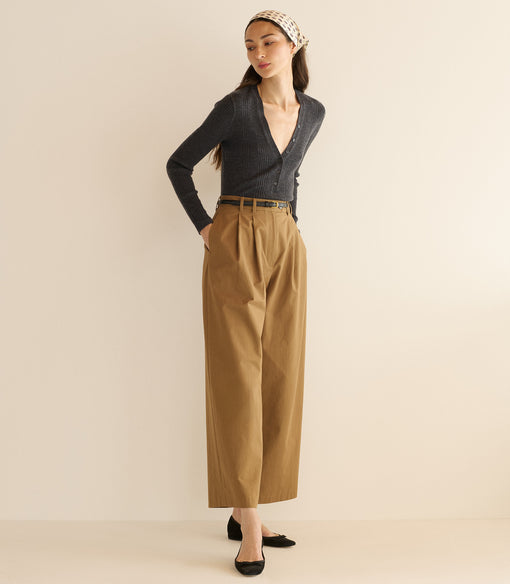 Woman wearing a dark blue cardigan and tan pants against a beige background