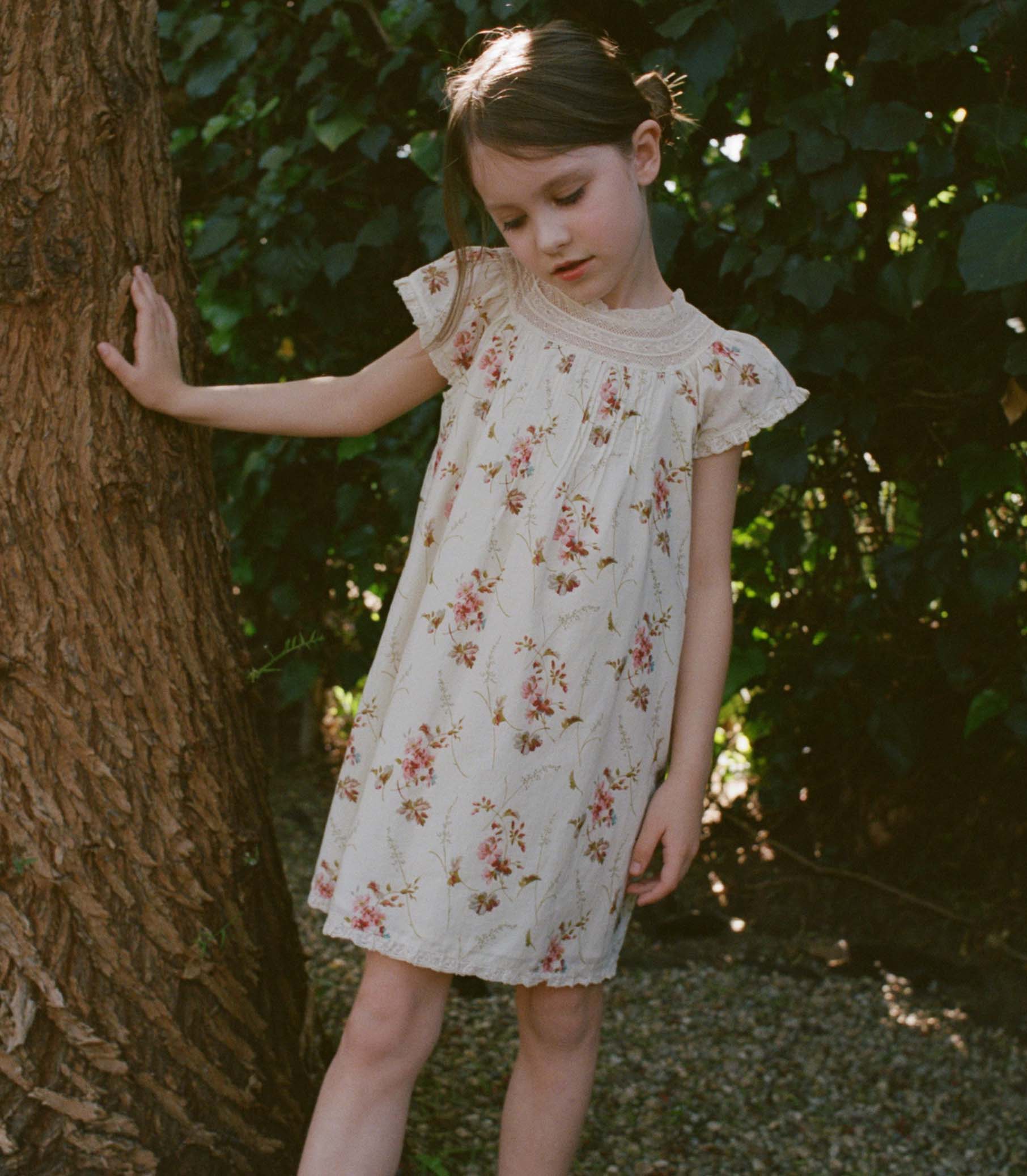 Young girl in a floral dress standing next to a tree in a natural setting