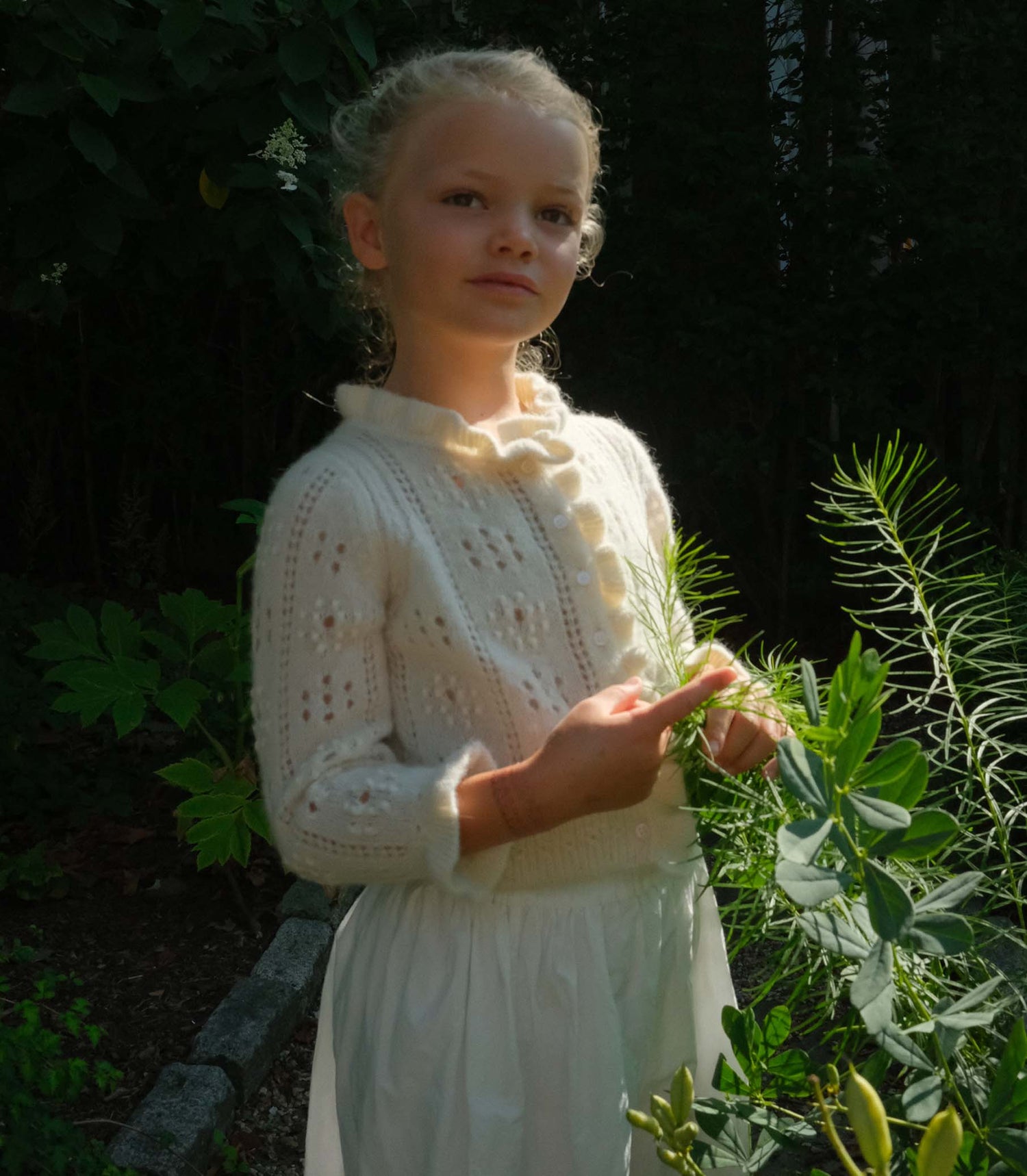Young girl in a white dress standing among plants