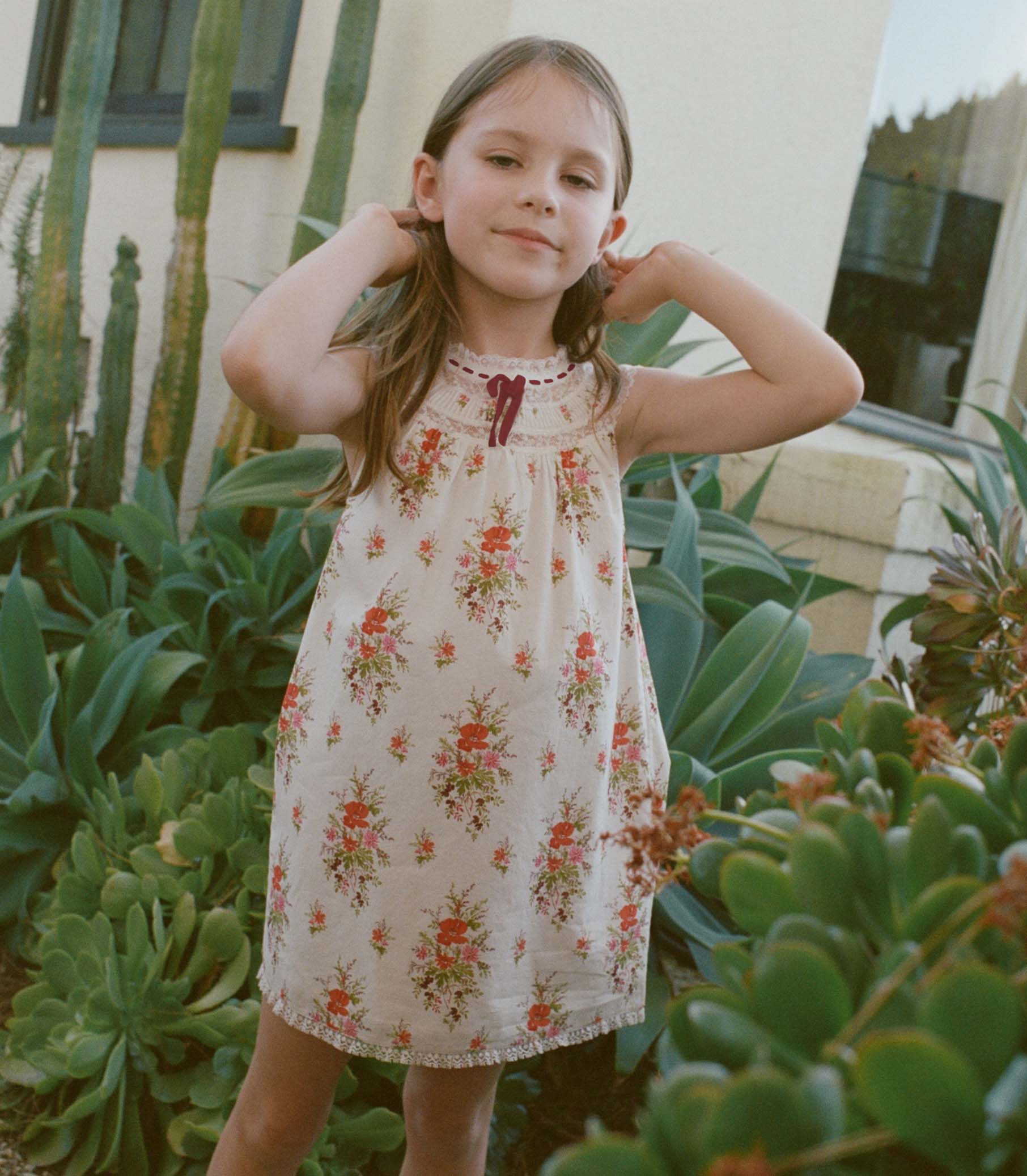 Young girl in a floral dress standing among plants