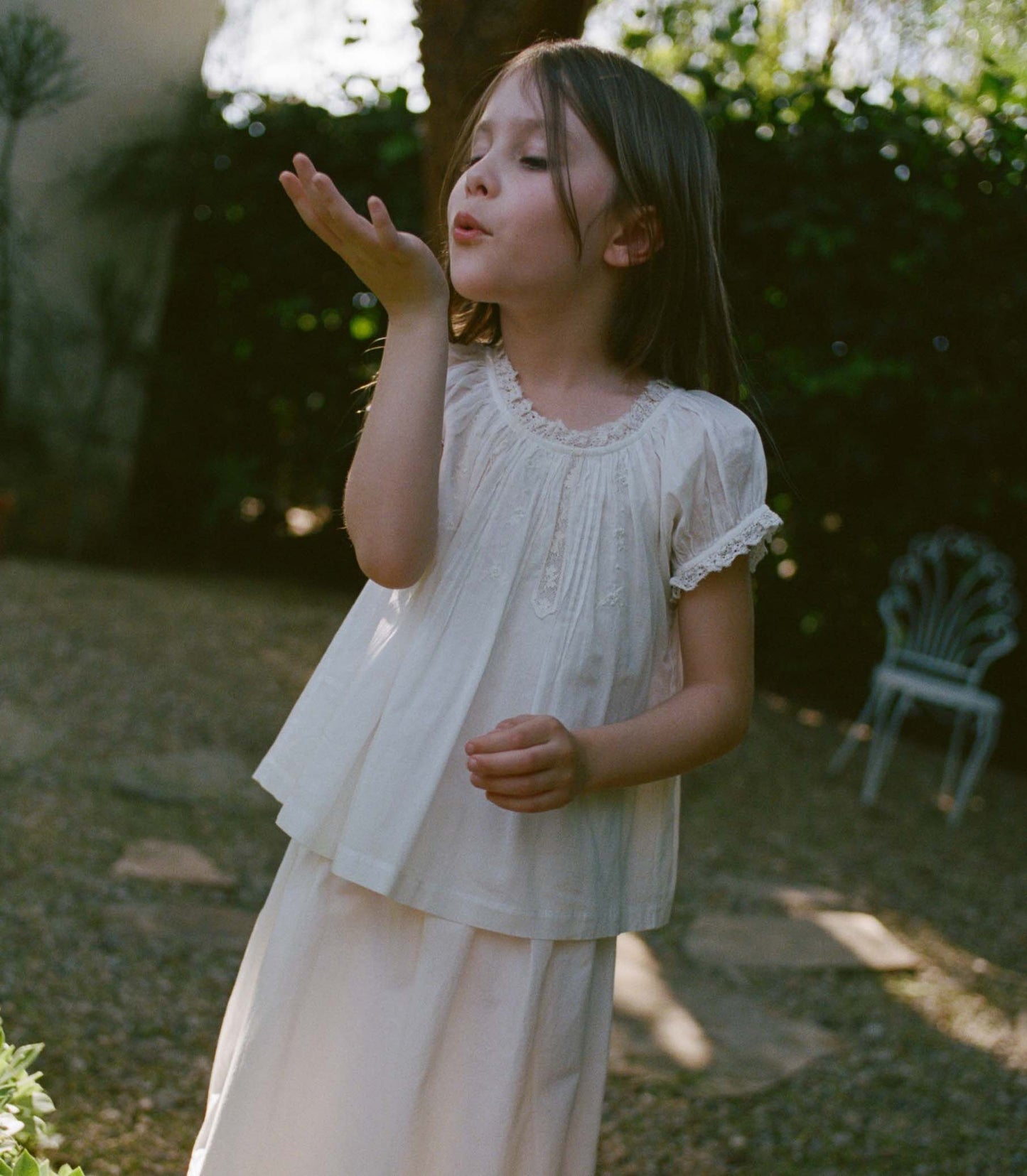 Young girl in a white blouse blowing bubbles outdoors