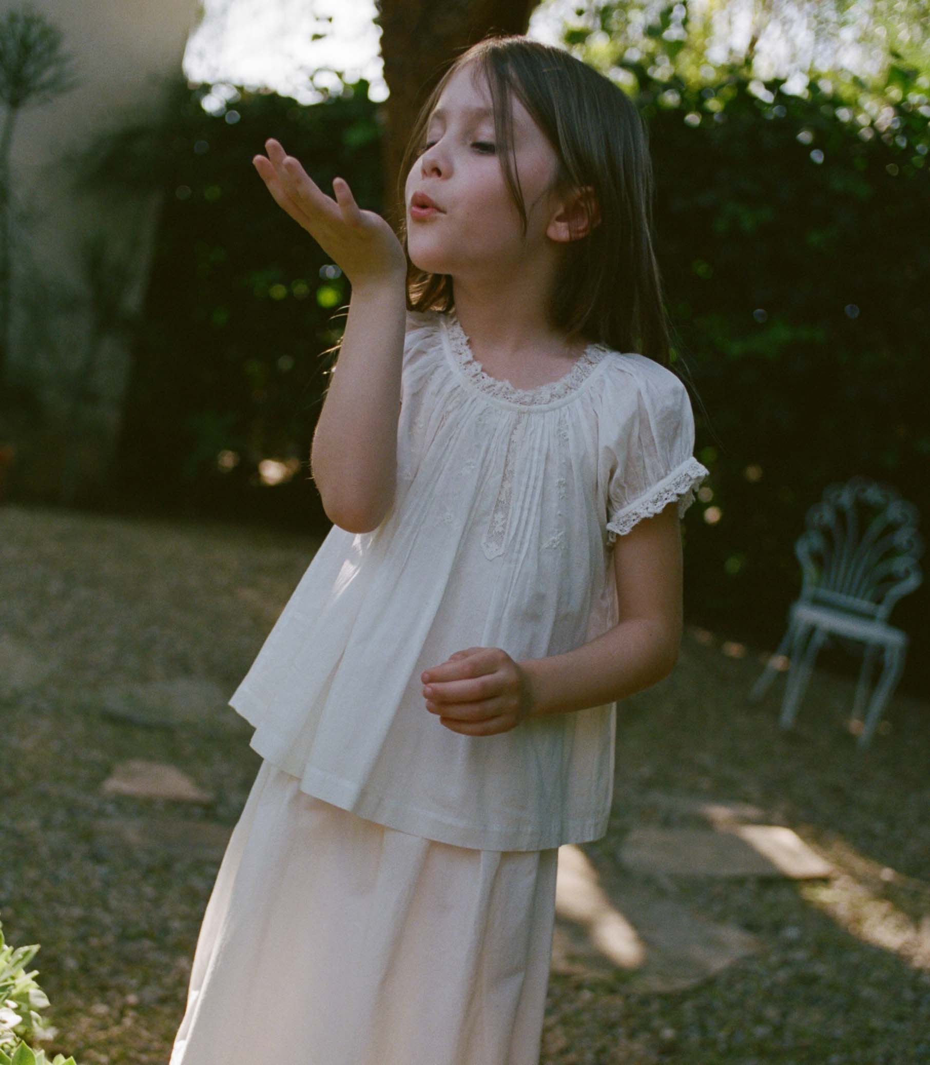 Young girl in a white blouse blowing bubbles outdoors