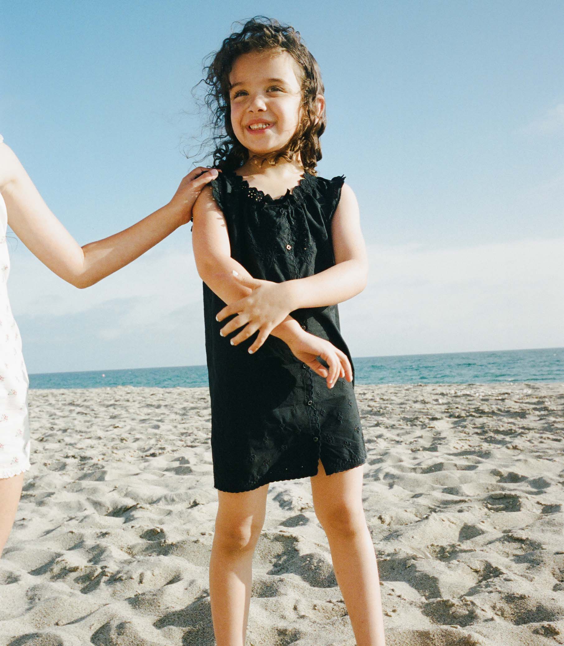 Young girl in a black dress standing on a sandy beach with ocean view