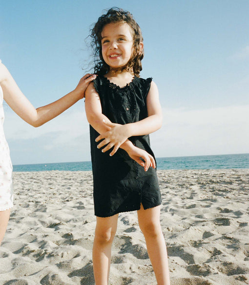 Young girl in a black dress standing on a sandy beach with ocean view