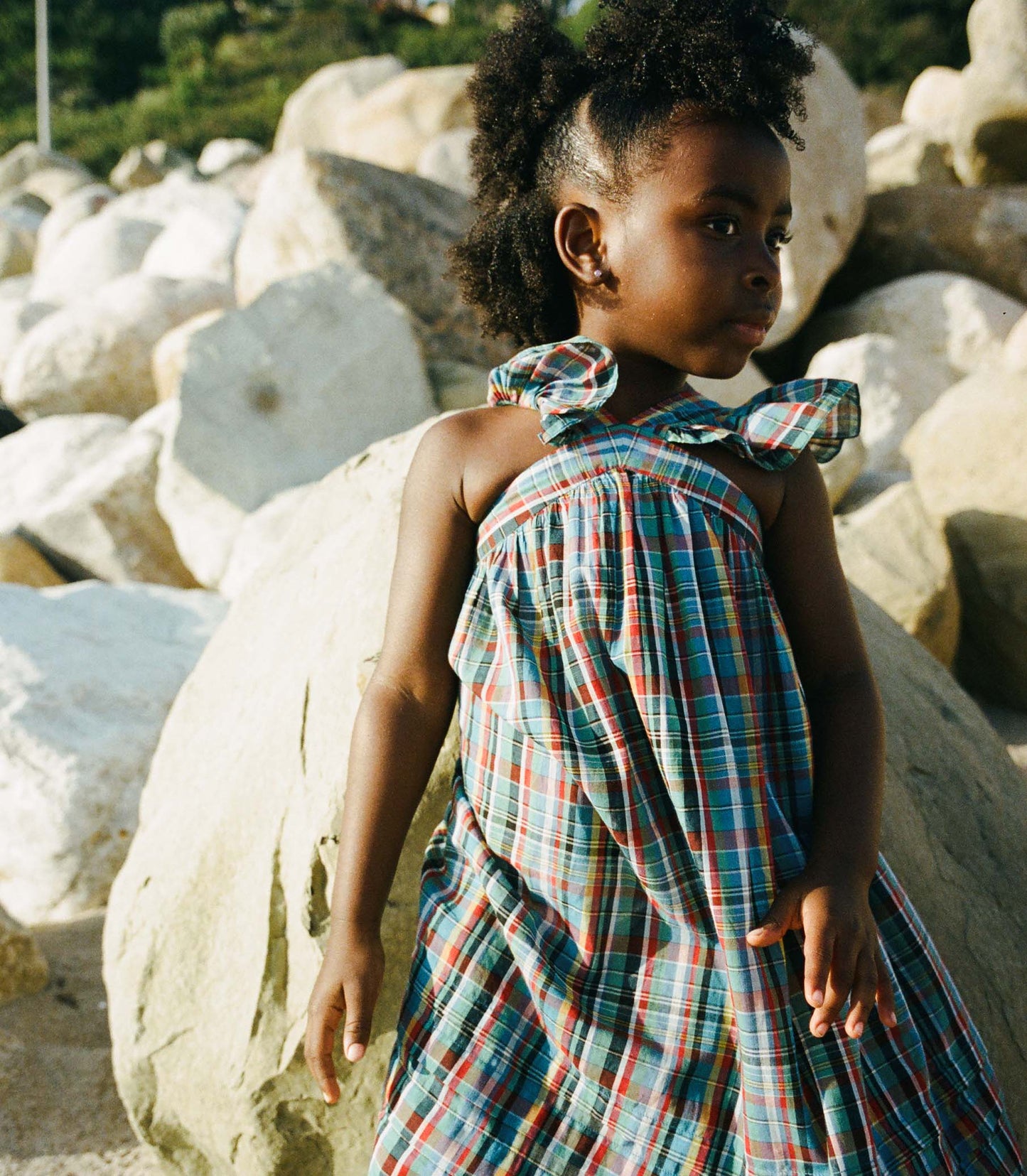 Young girl in a plaid dress standing among large rocks.