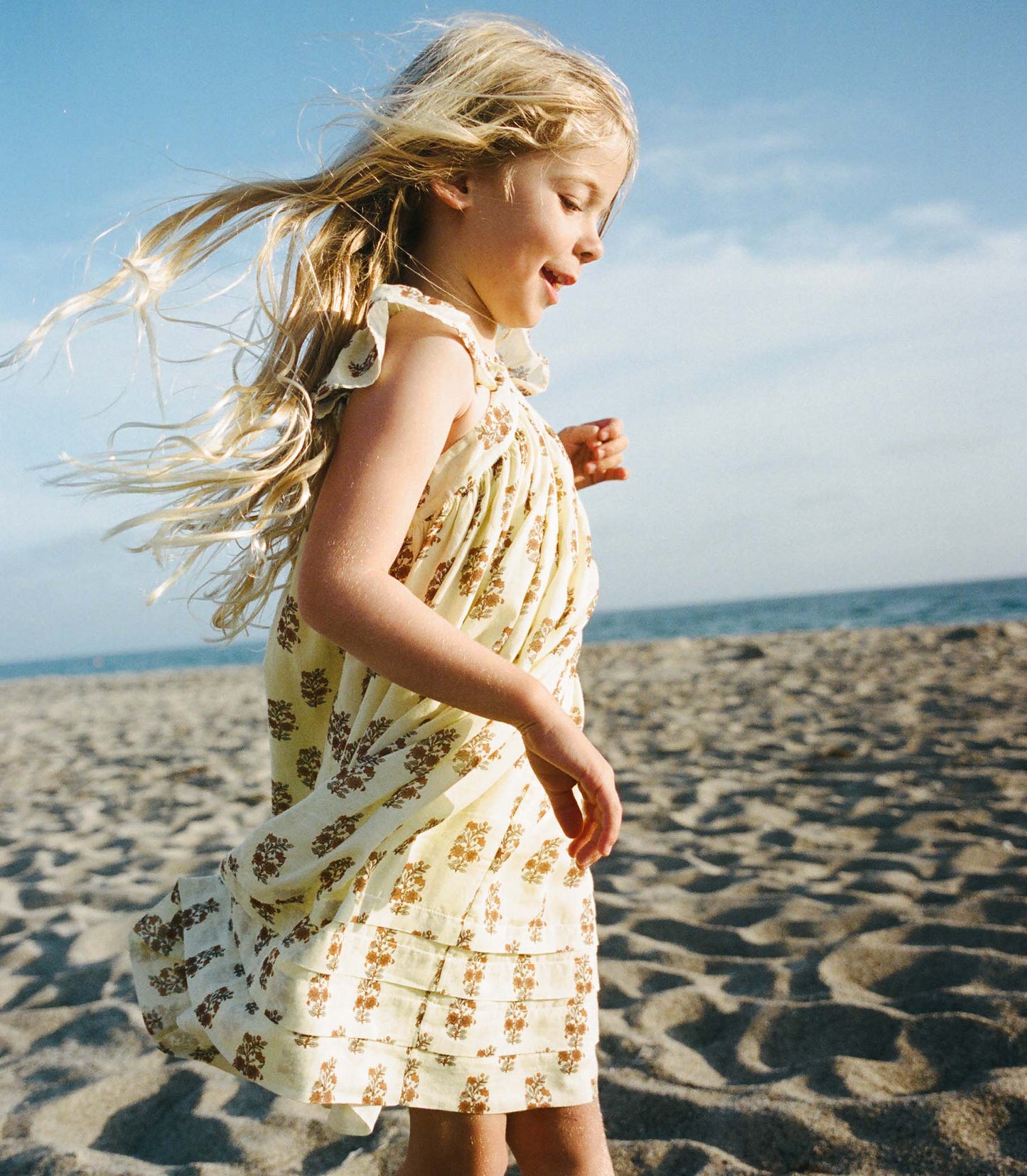 Young girl in a floral dress standing on a sandy beach with ocean view
