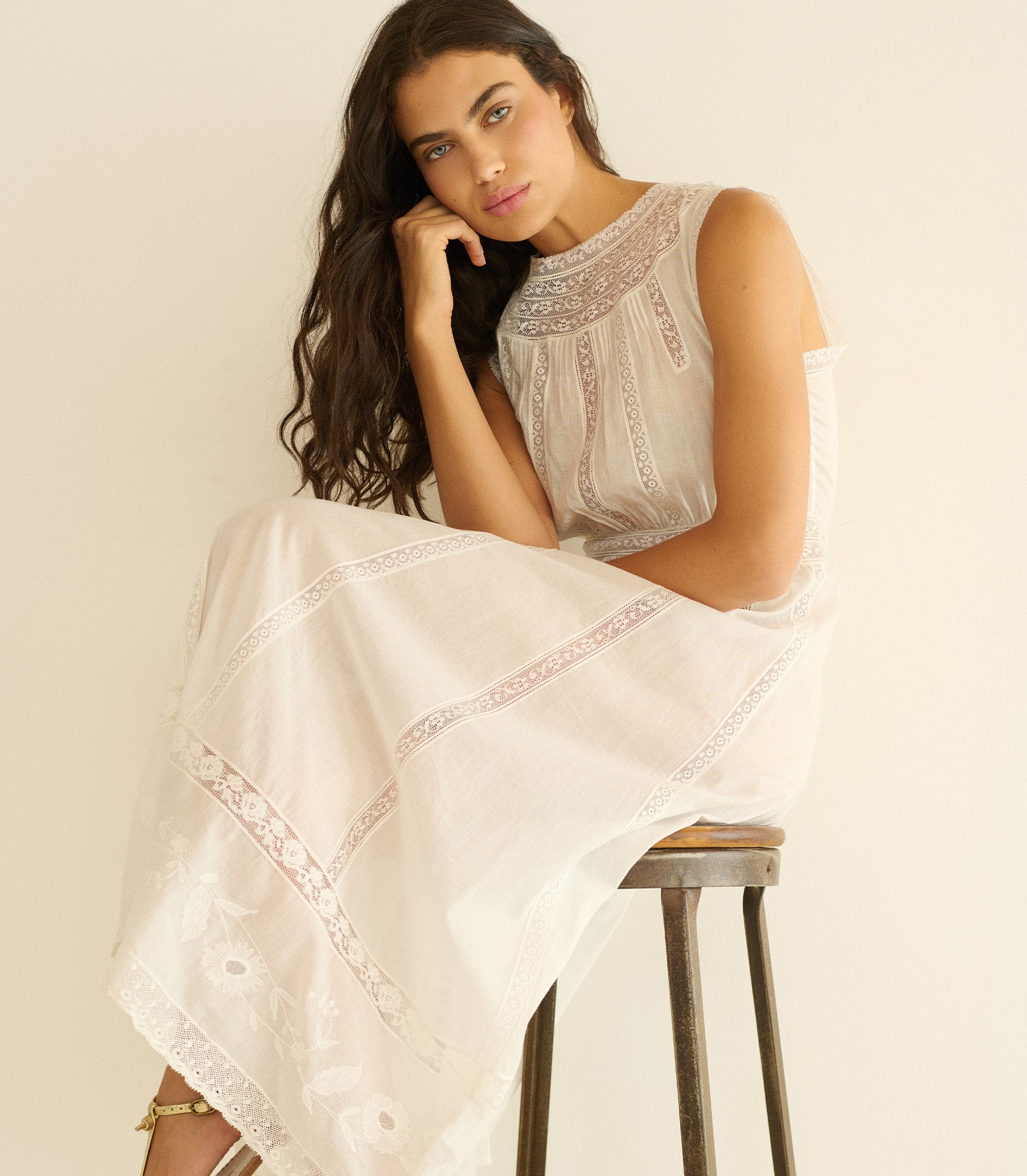 Woman sitting on a stool wearing a white lace dress against a plain background 1
