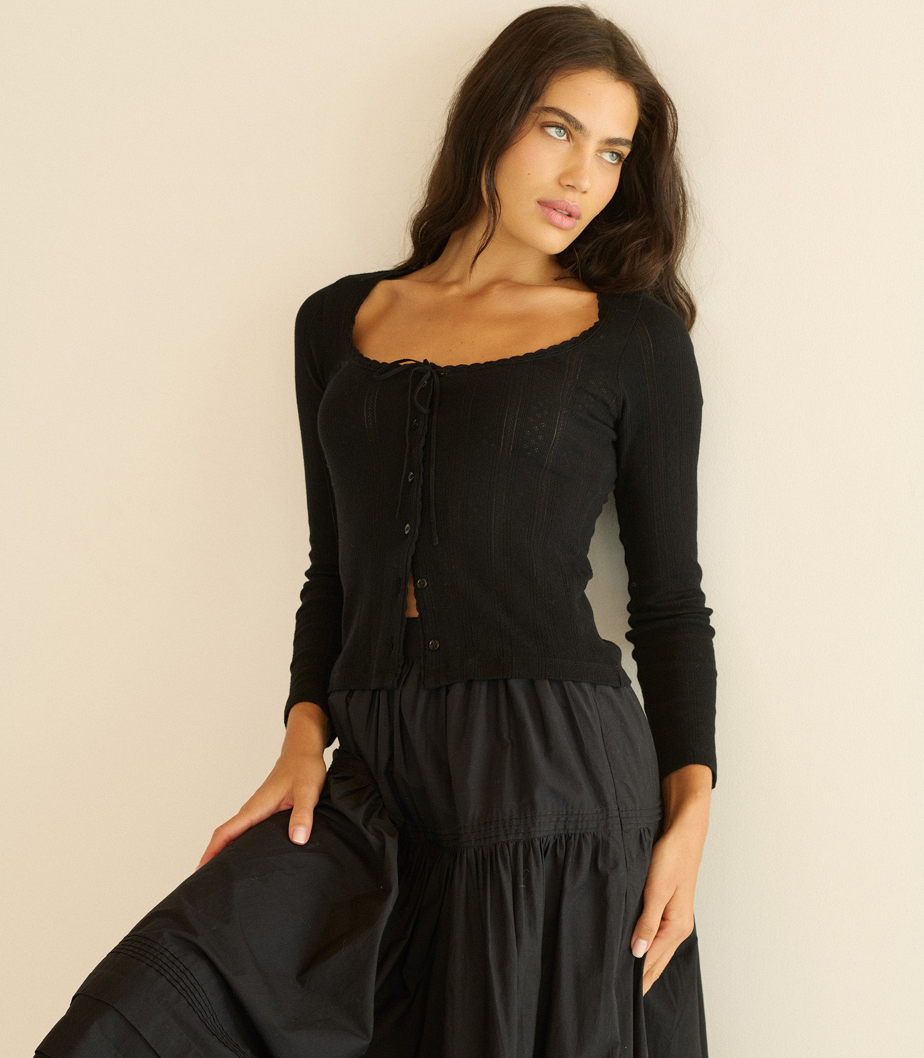 Woman wearing a black top with long sleeves and a black skirt against a beige background