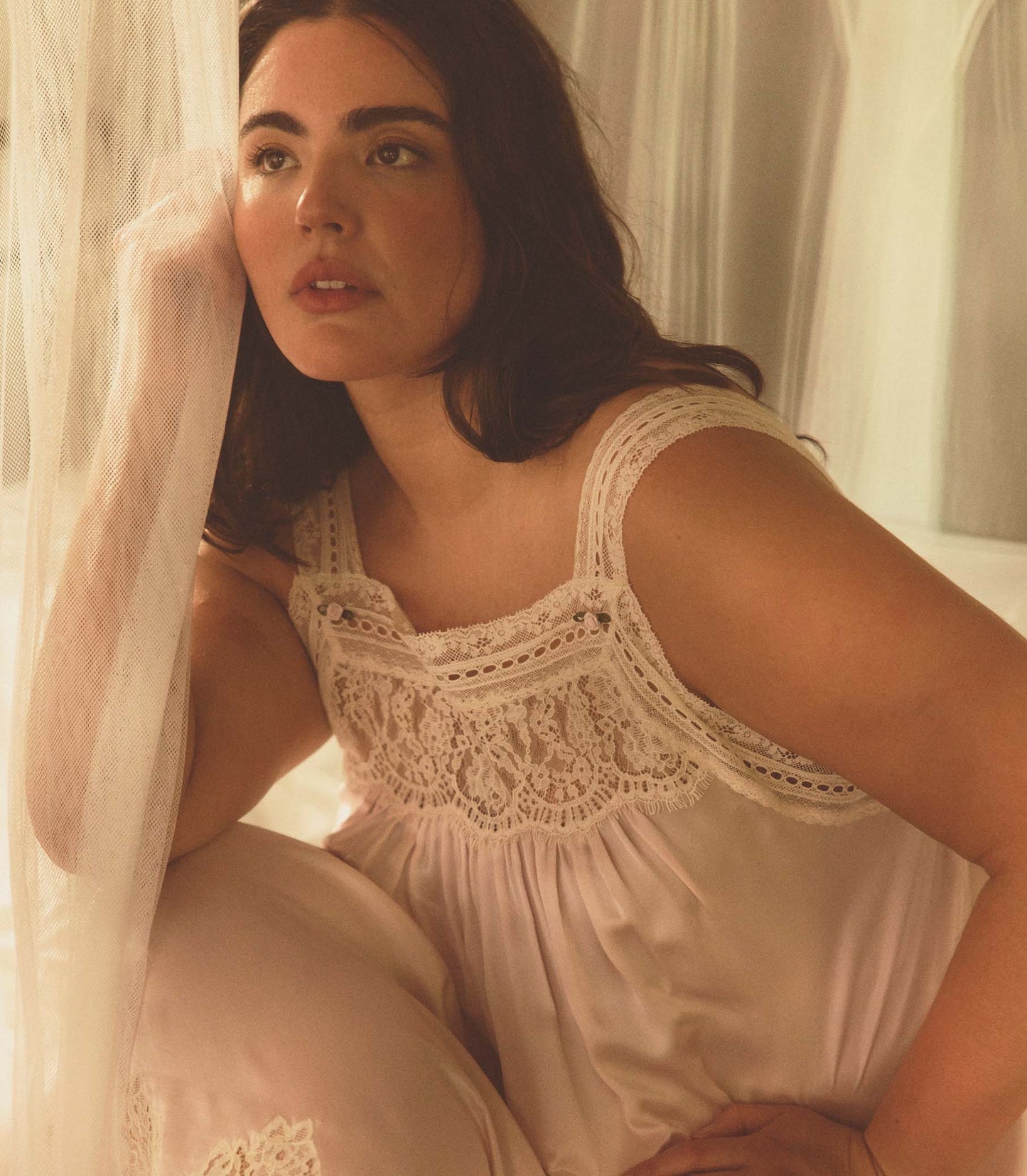 Woman wearing a lace-trimmed dress sitting in a softly lit room.