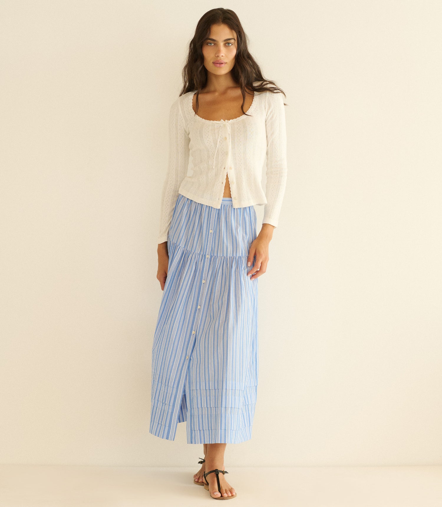 Woman wearing a white top and blue striped skirt on a beige background