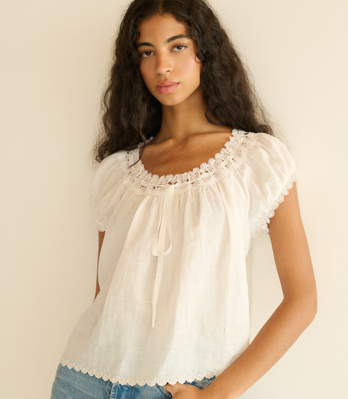 Woman wearing a white blouse with lace details against a beige background