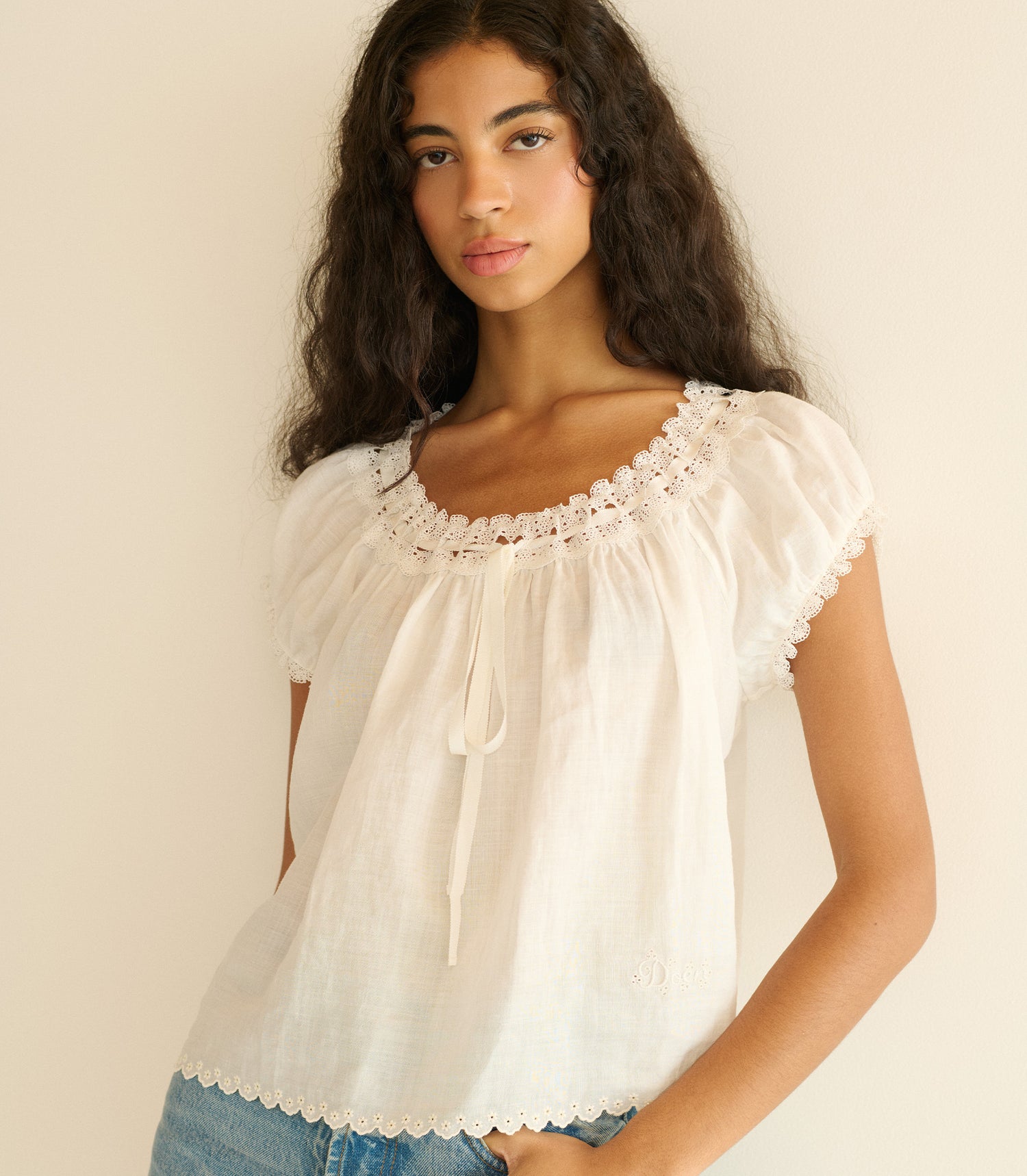 Woman wearing a white blouse with lace details against a beige background