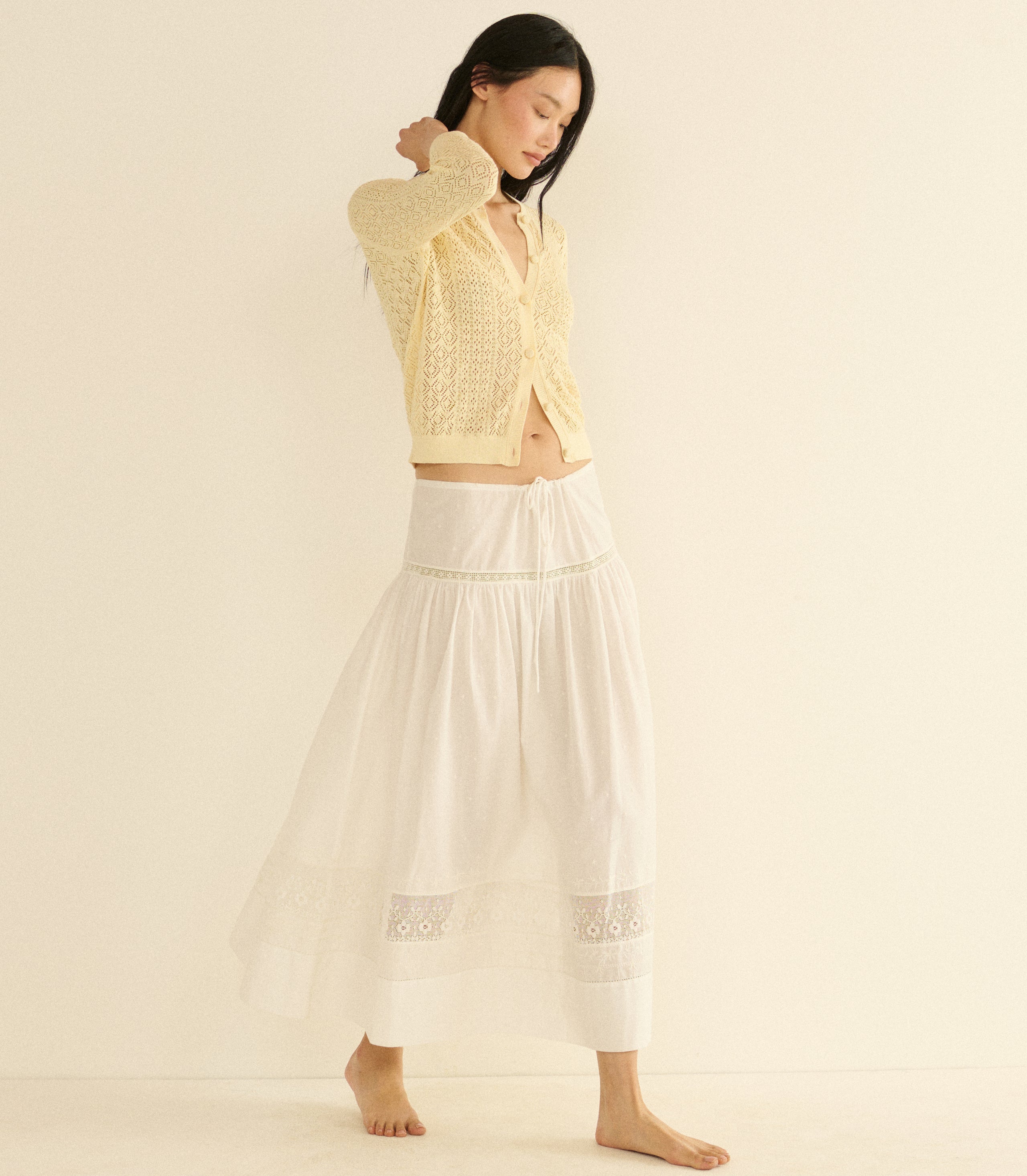 Woman wearing a yellow textured cardigan and white skirt on a beige background