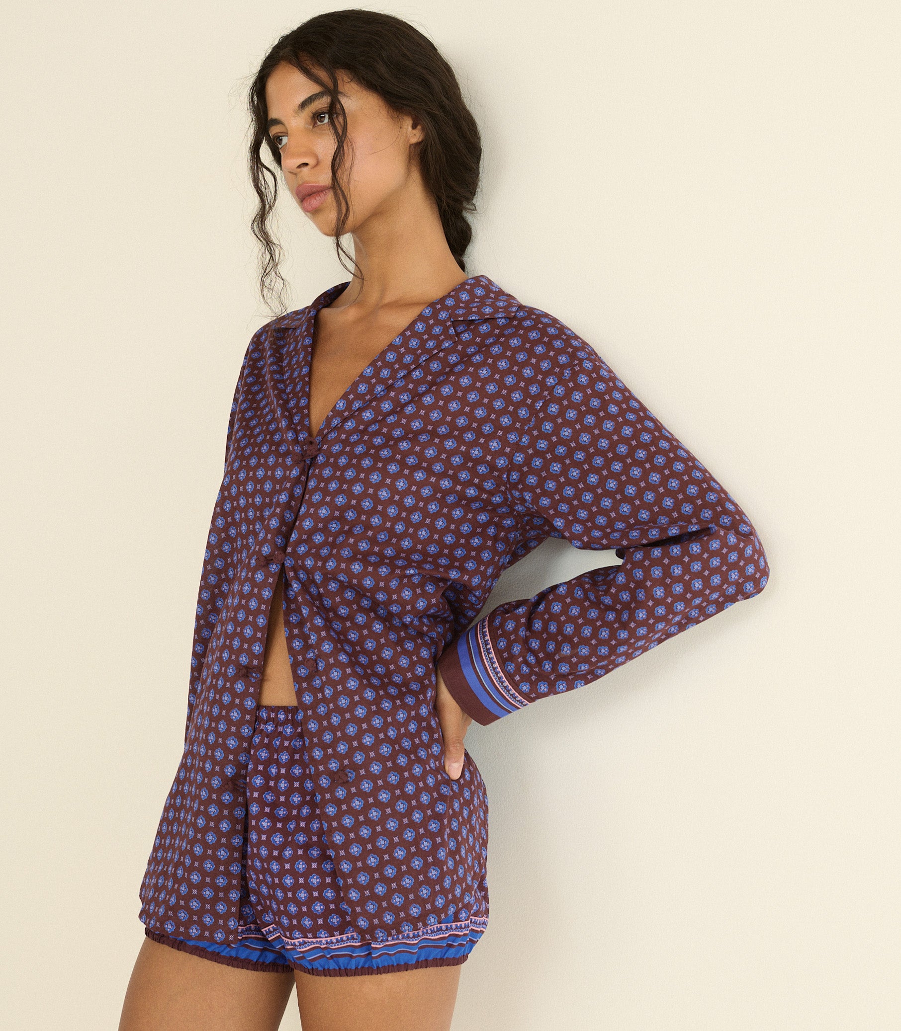 A woman wearing a purple and blue foulard long-sleeve top with striped cuffs, posed against a plain off-white background.