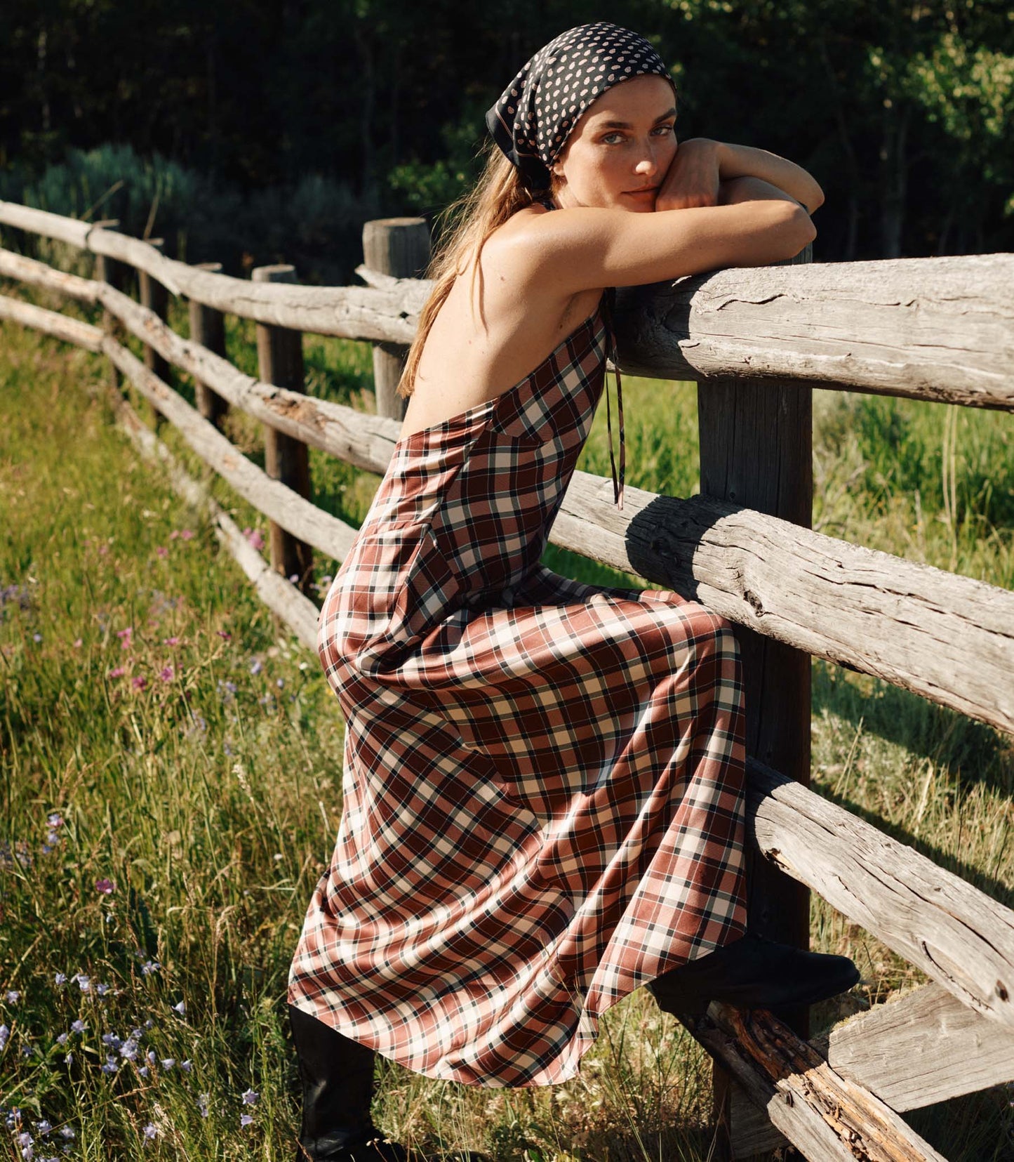 Woman in a plaid dress sitting on a wooden fence in a natural setting