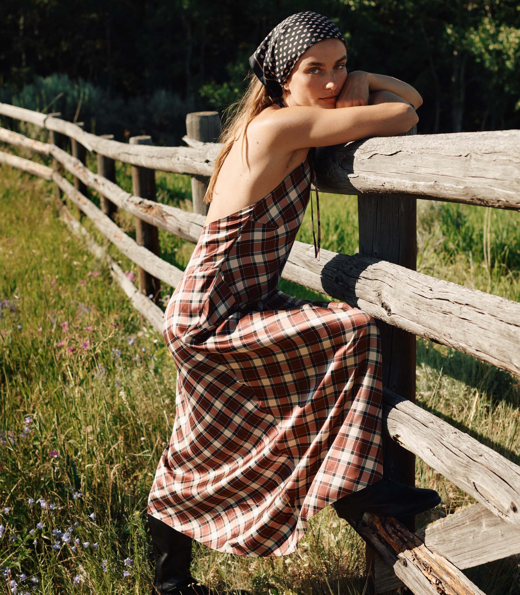 Woman in a plaid dress sitting on a wooden fence in a natural setting 1